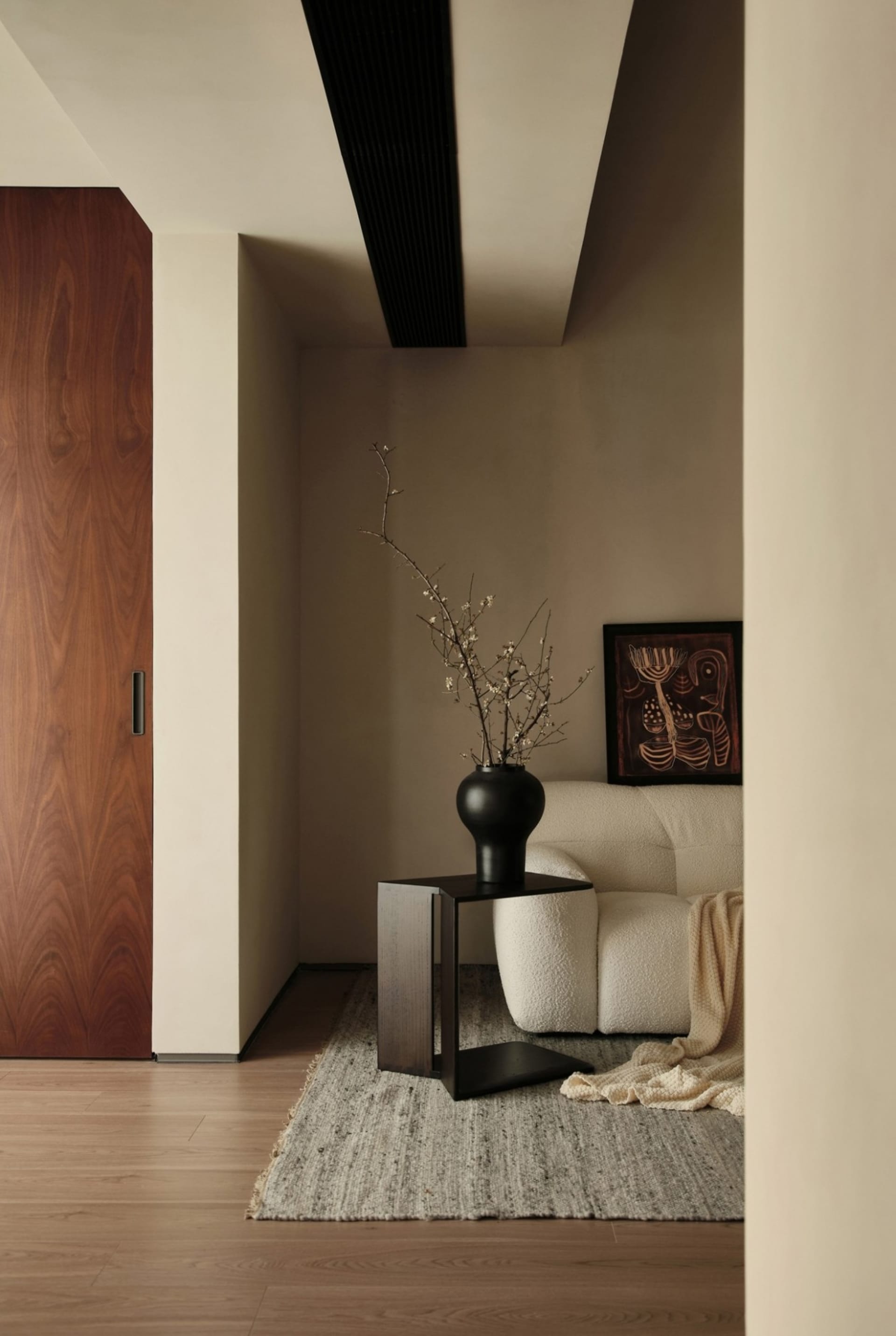 A modern living room with a cream-colored sofa, a black vase with a branch, and a framed artwork.