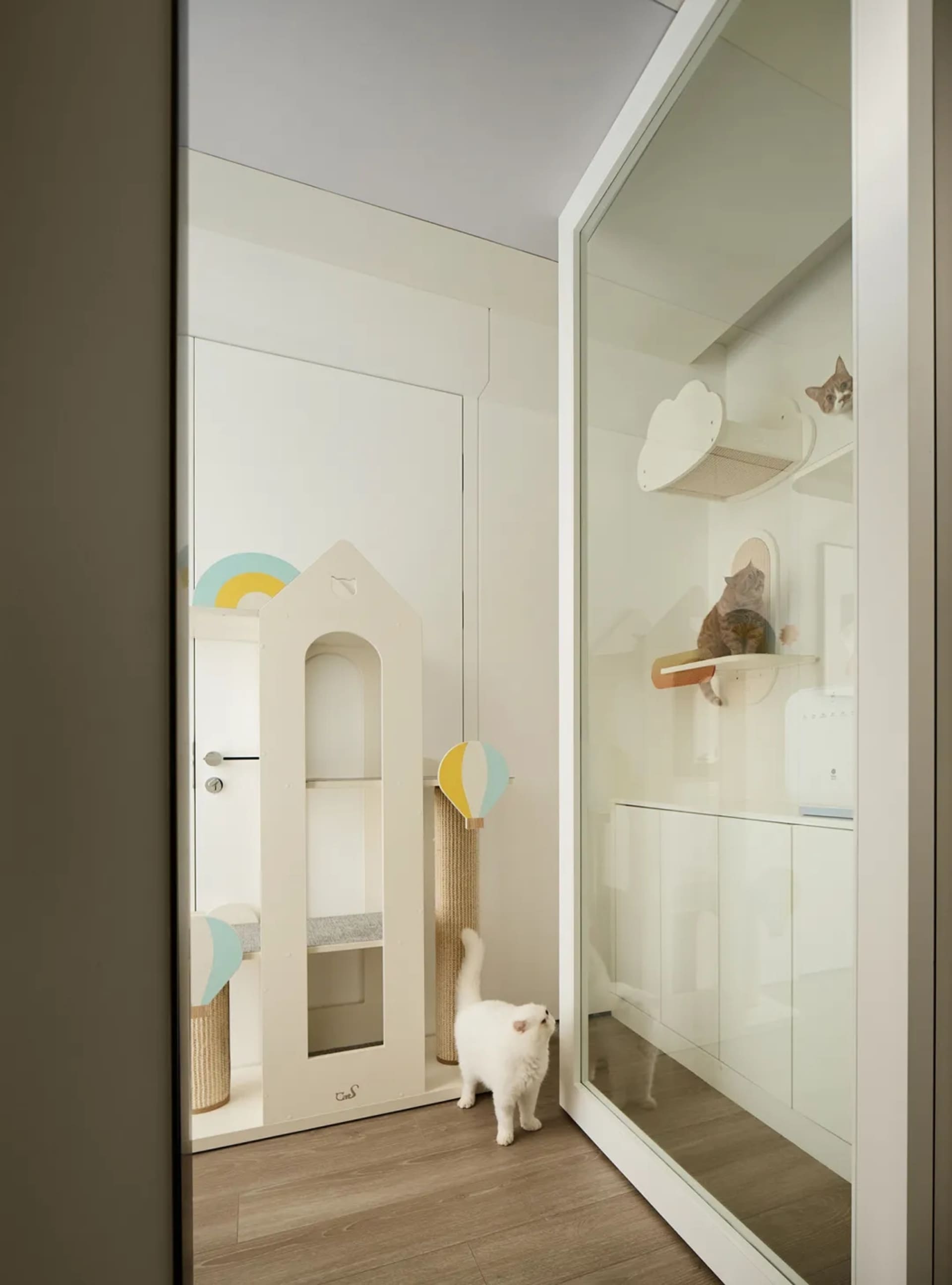 A white indoor cat playroom featuring climbing structures and shelves with a white cat inside.
