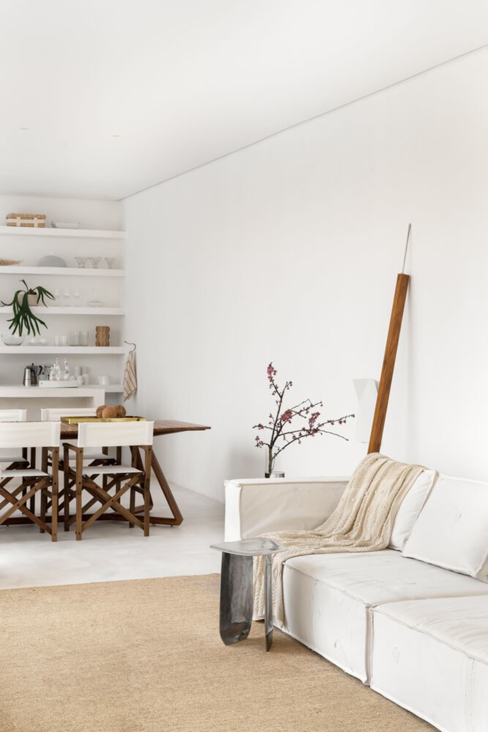 A minimalist living room with a white sofa, wooden floor, and white walls, featuring a wooden stand and a plant.