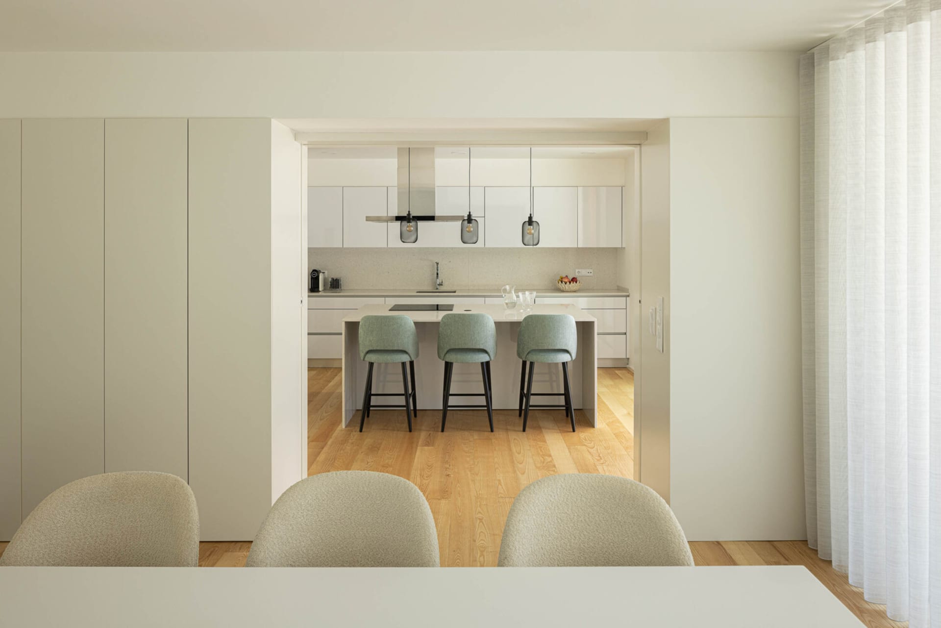 Modern kitchen featuring white cabinets, countertop, and bar stools with green accents.