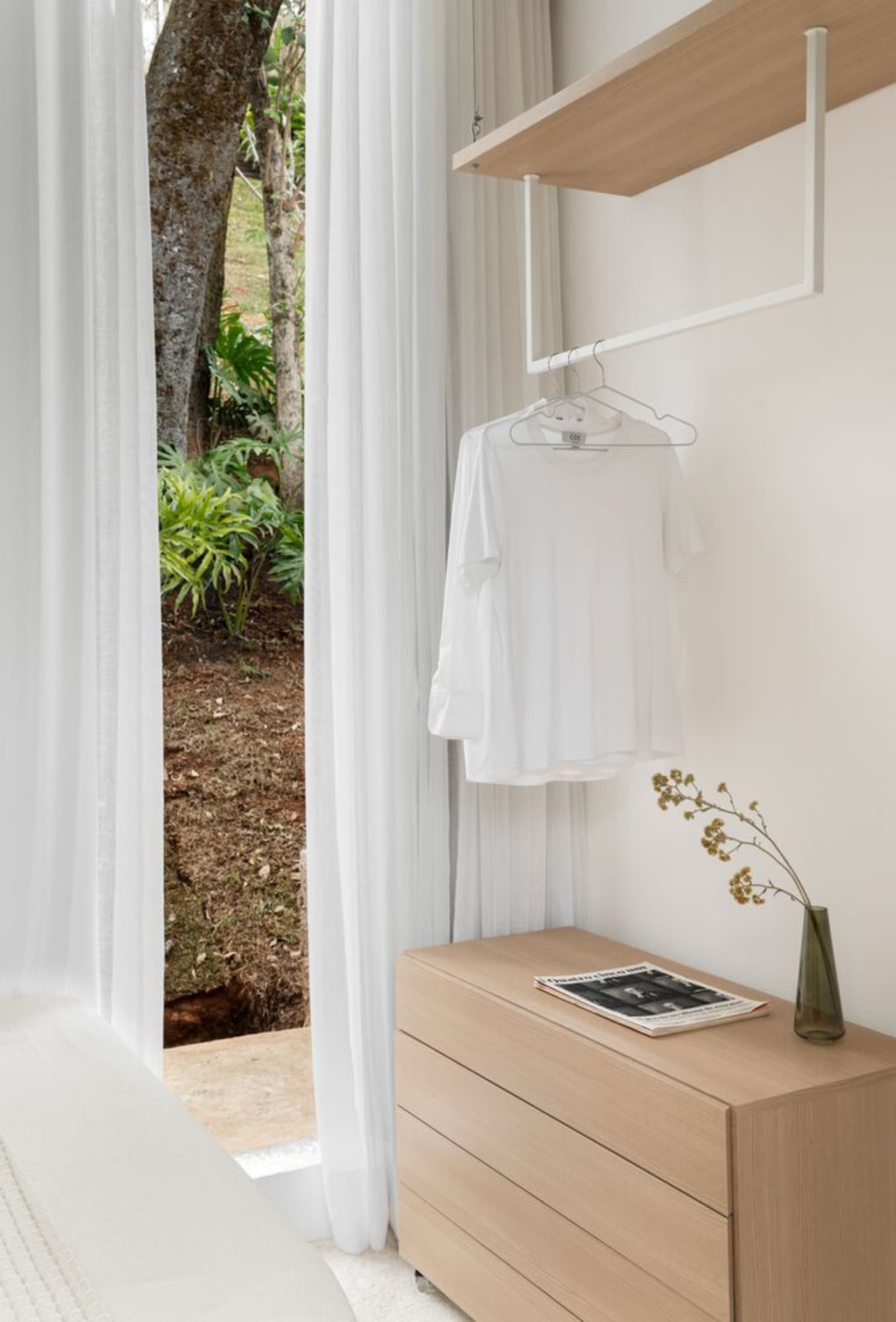 A minimalist closet interior featuring white Sherwood wood furniture and a white t-shirt hanging on a white hanger.