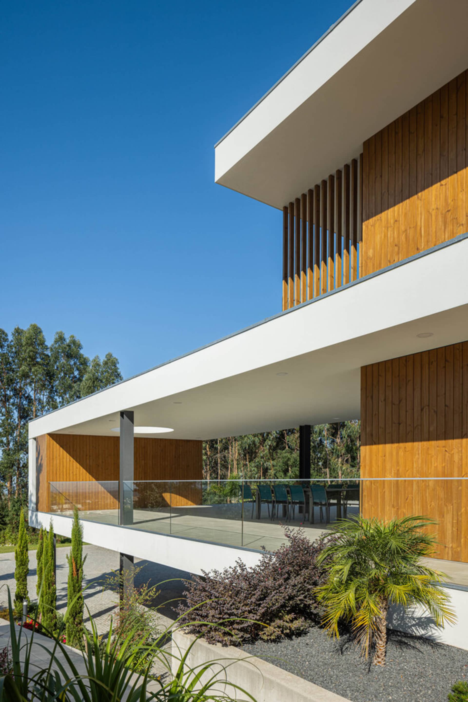 Contemporary house with wooden and glass exterior, featuring concrete patio and greenery.