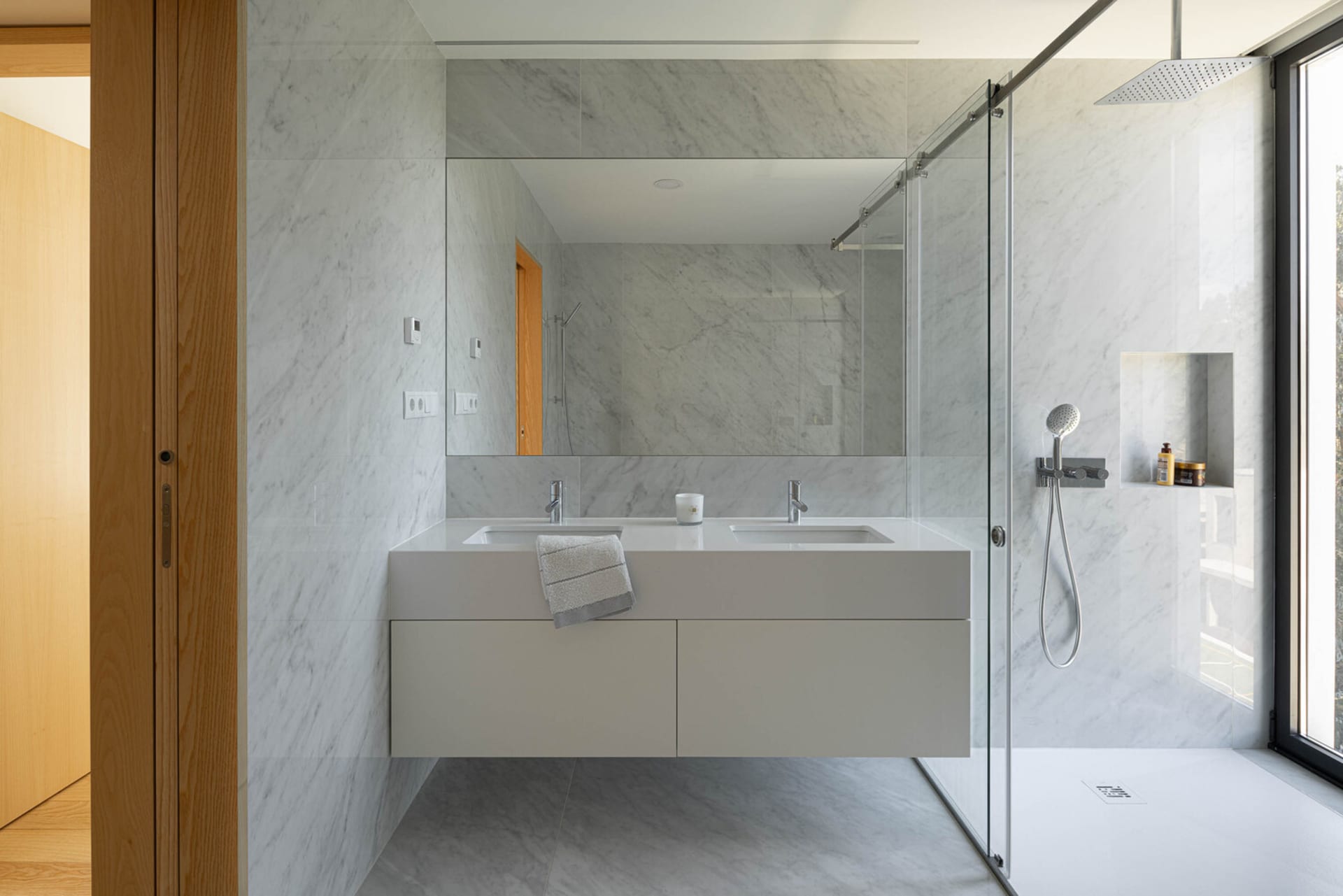 Contemporary marble bathroom with white porcelain sinks, white doors, and glass shower enclosure.