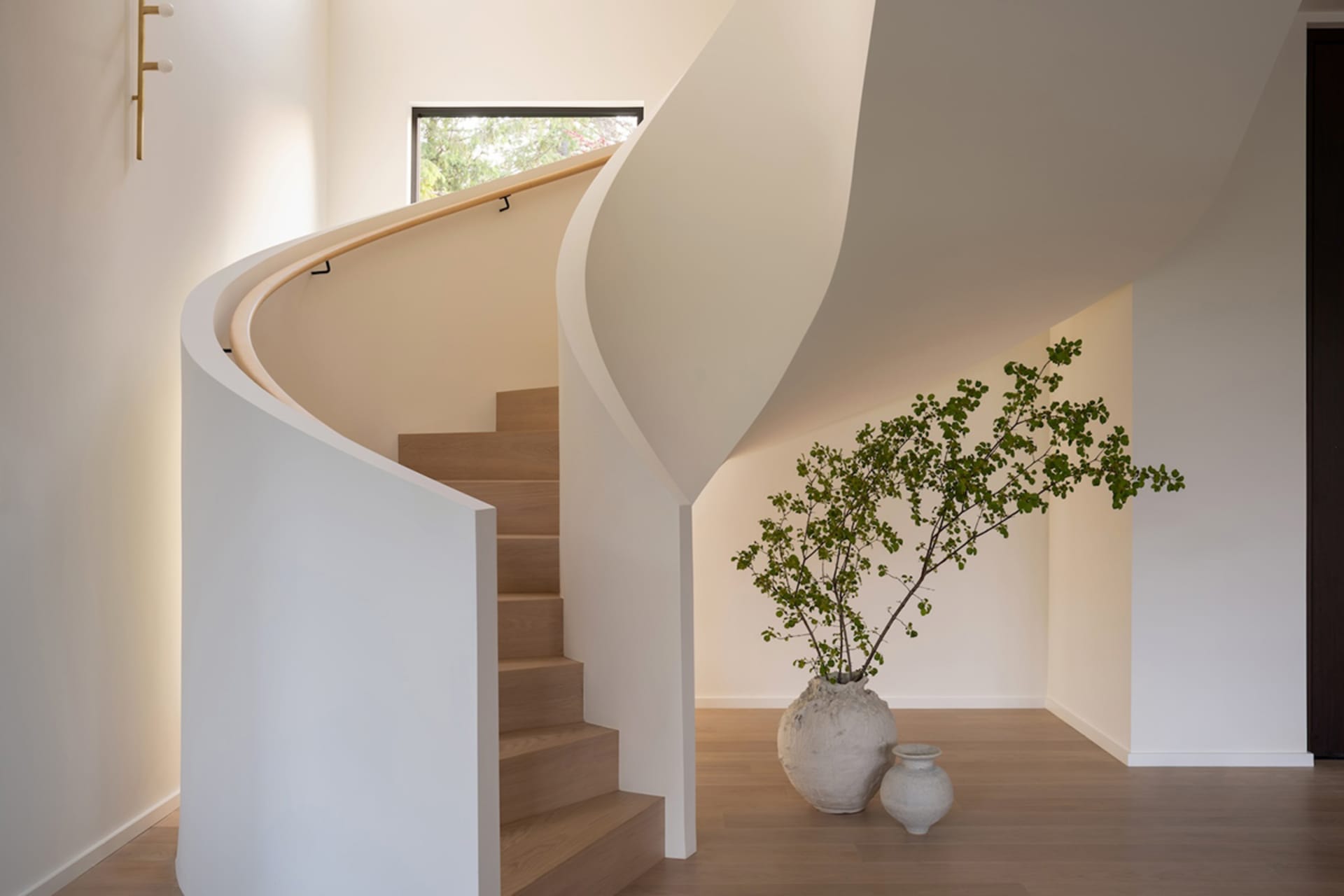 A modern minimalist staircase with a curved white handrail and wooden steps.