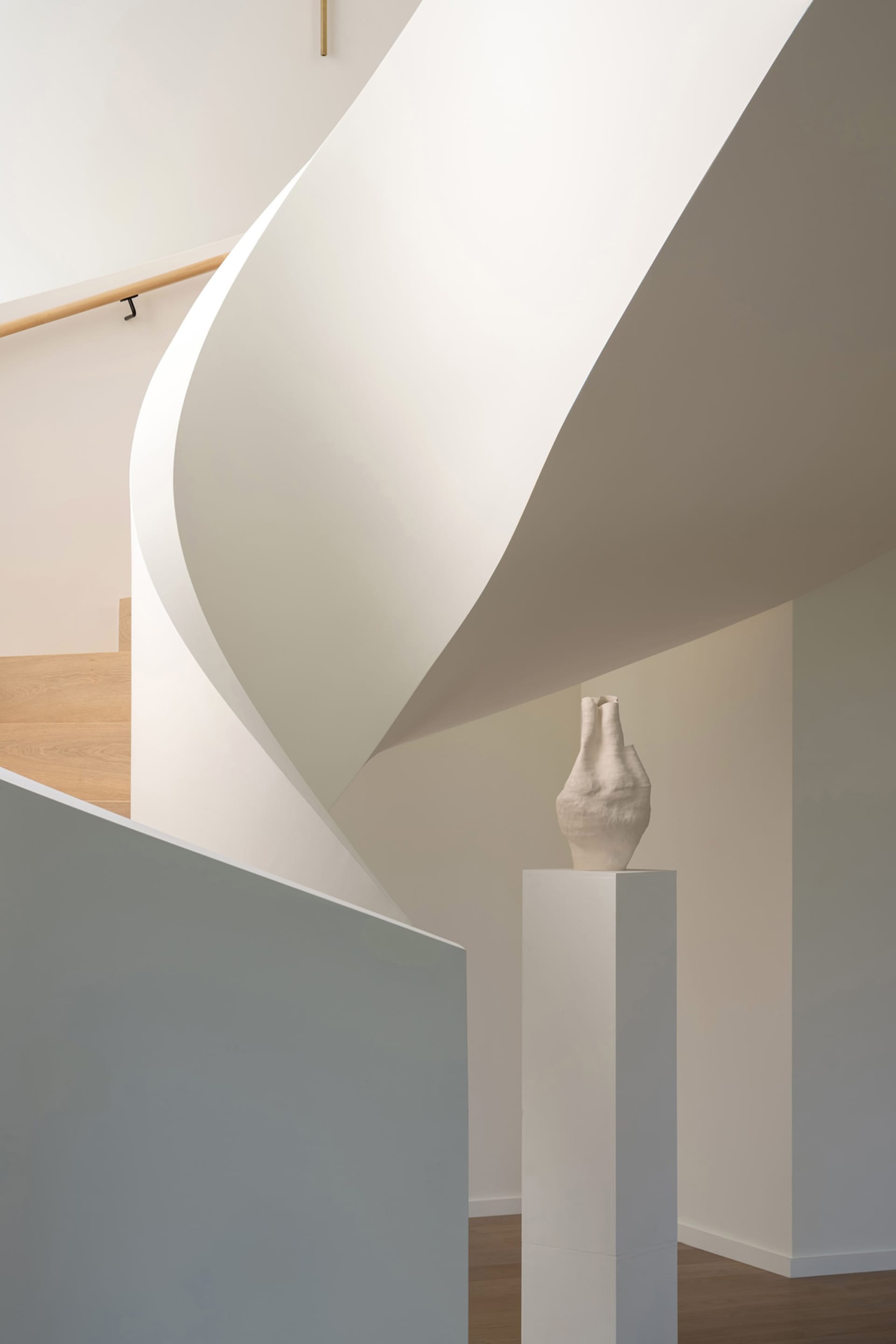 A modern minimalist staircase made of concrete with a white curved wall and wooden steps.