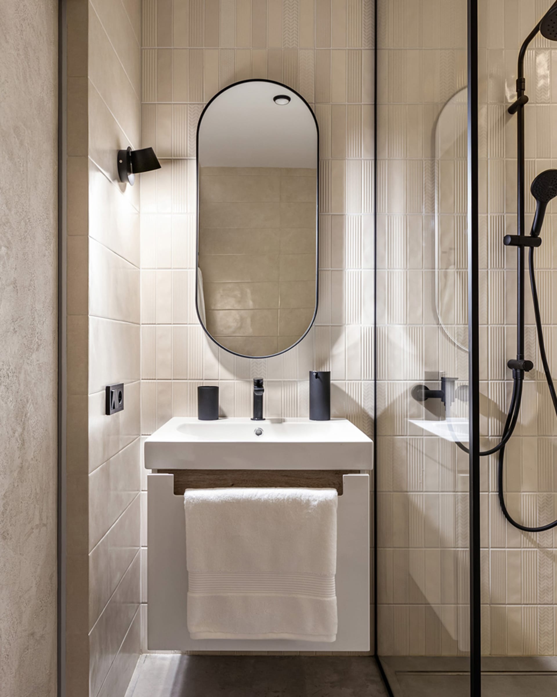 Minimalist bathroom with modern fixtures, oval-shaped mirror, and white ceramic tiles on walls and floor.