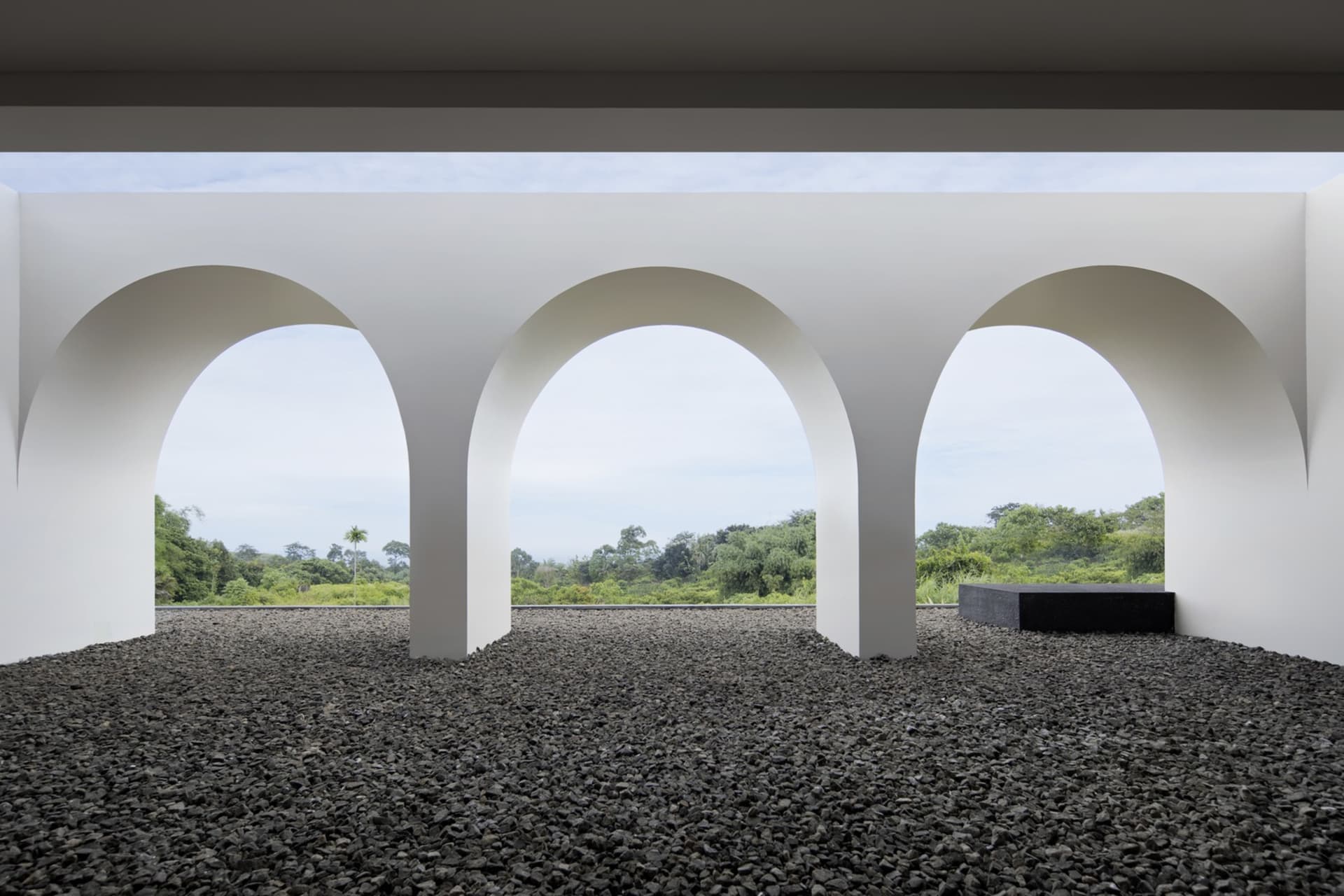 A view through an arched corridor of a modern interior with a concrete floor and natural landscape outside.