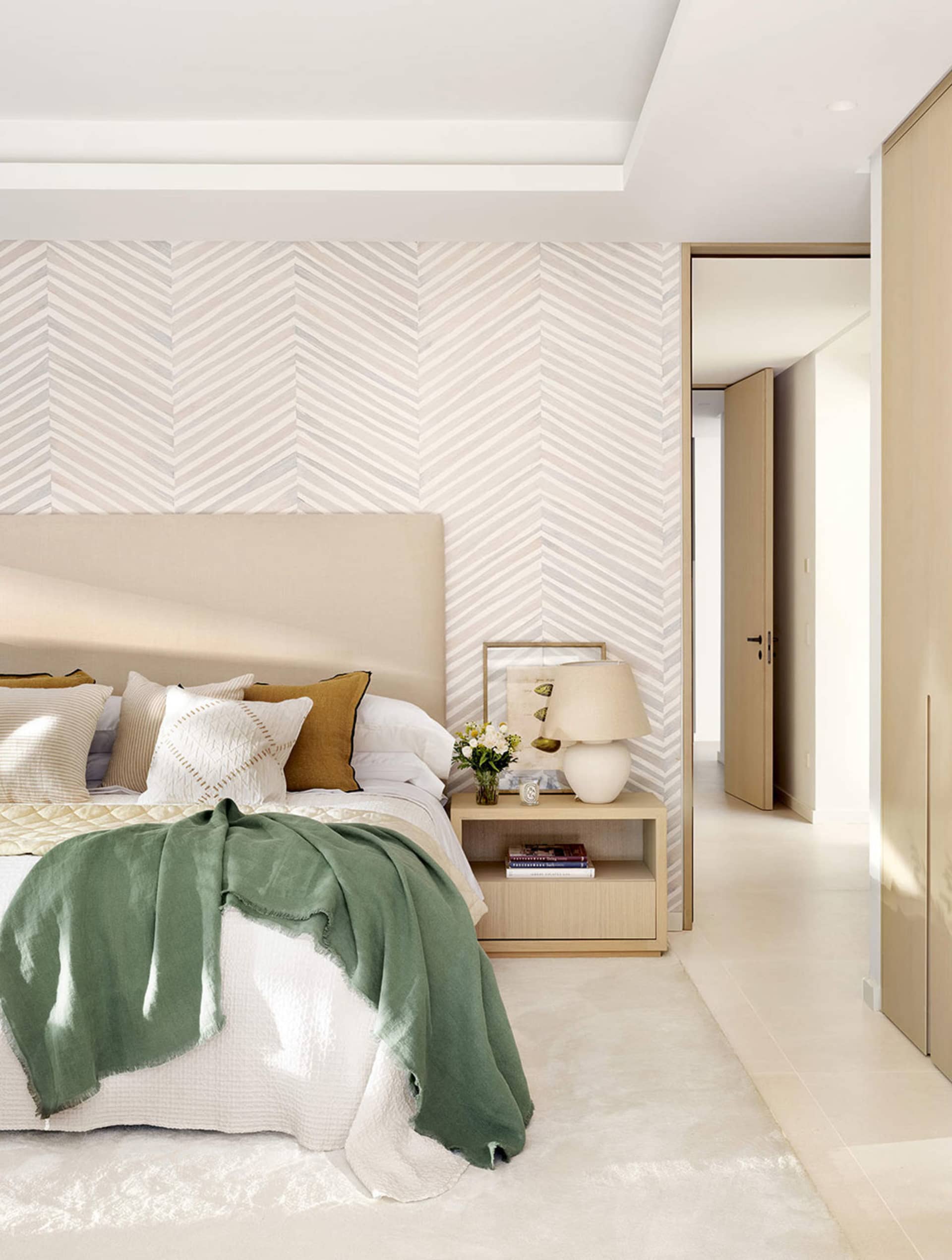 Modern minimalist bedroom featuring a bed with green and white textiles, a wooden nightstand, and a herringbone-patterned wal