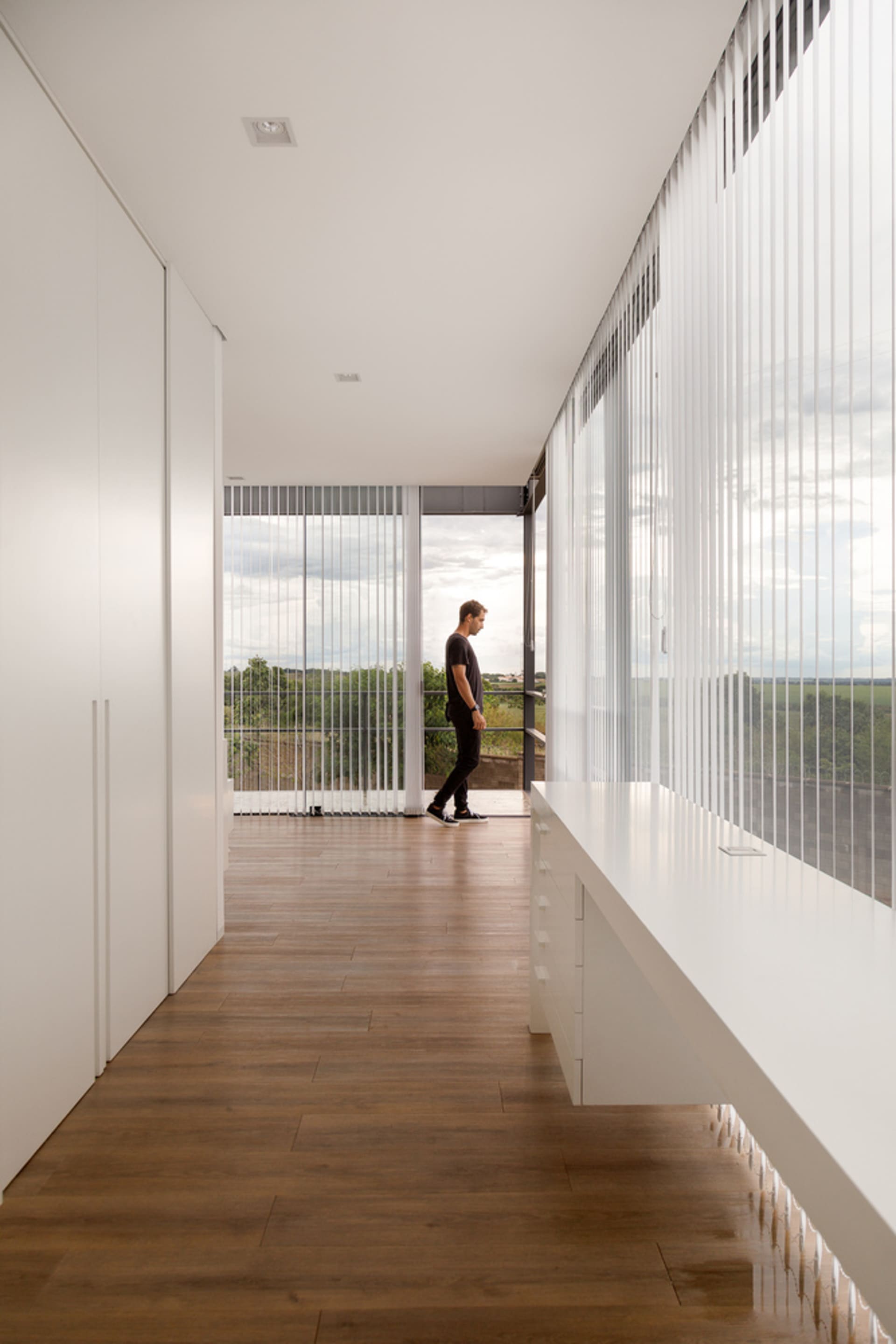 Man standing in a modern residential interior with large glass walls, showcasing a minimalist design with natural light.