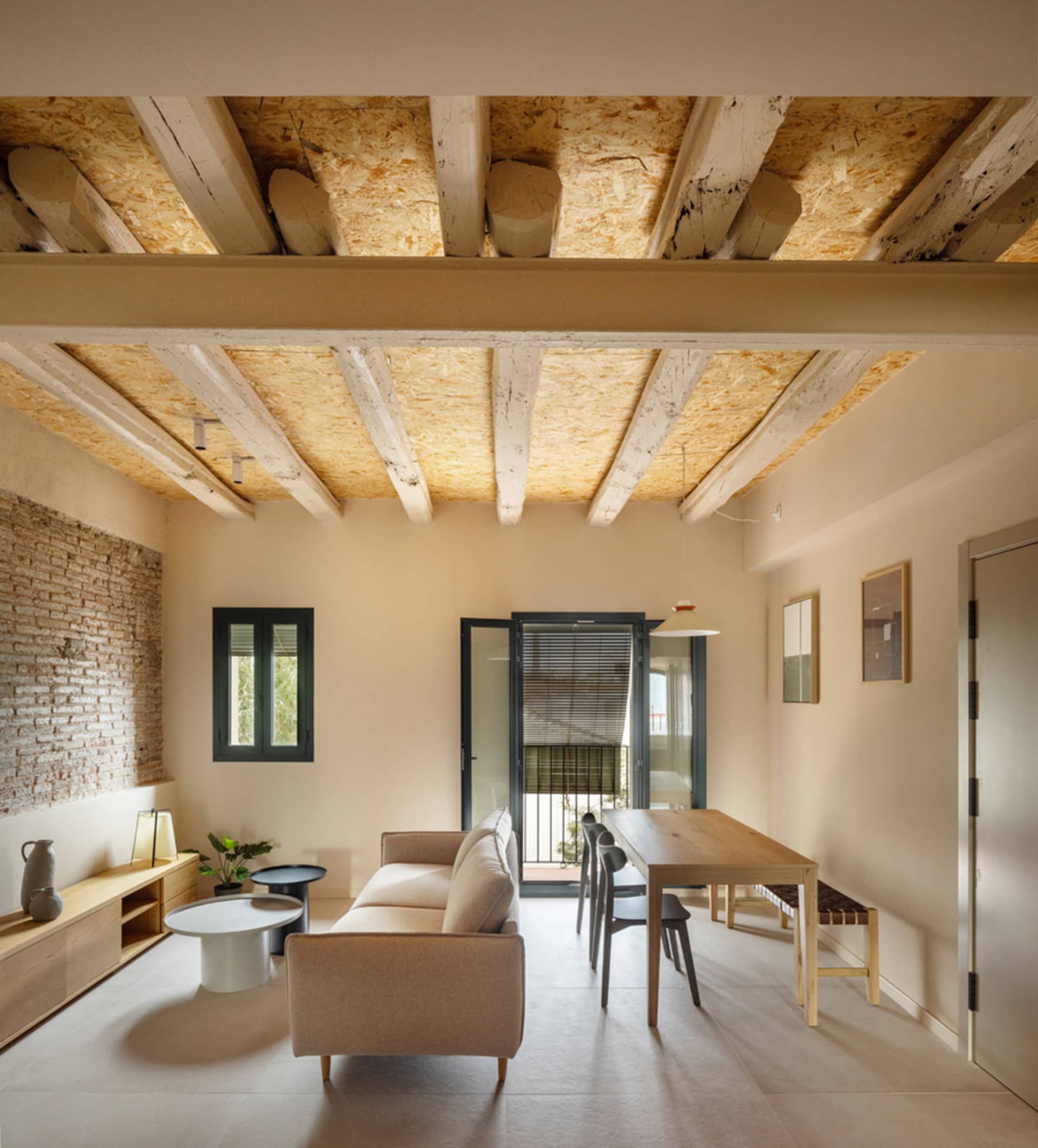 A minimalist living room with wooden furniture and exposed wooden beams on the ceiling.