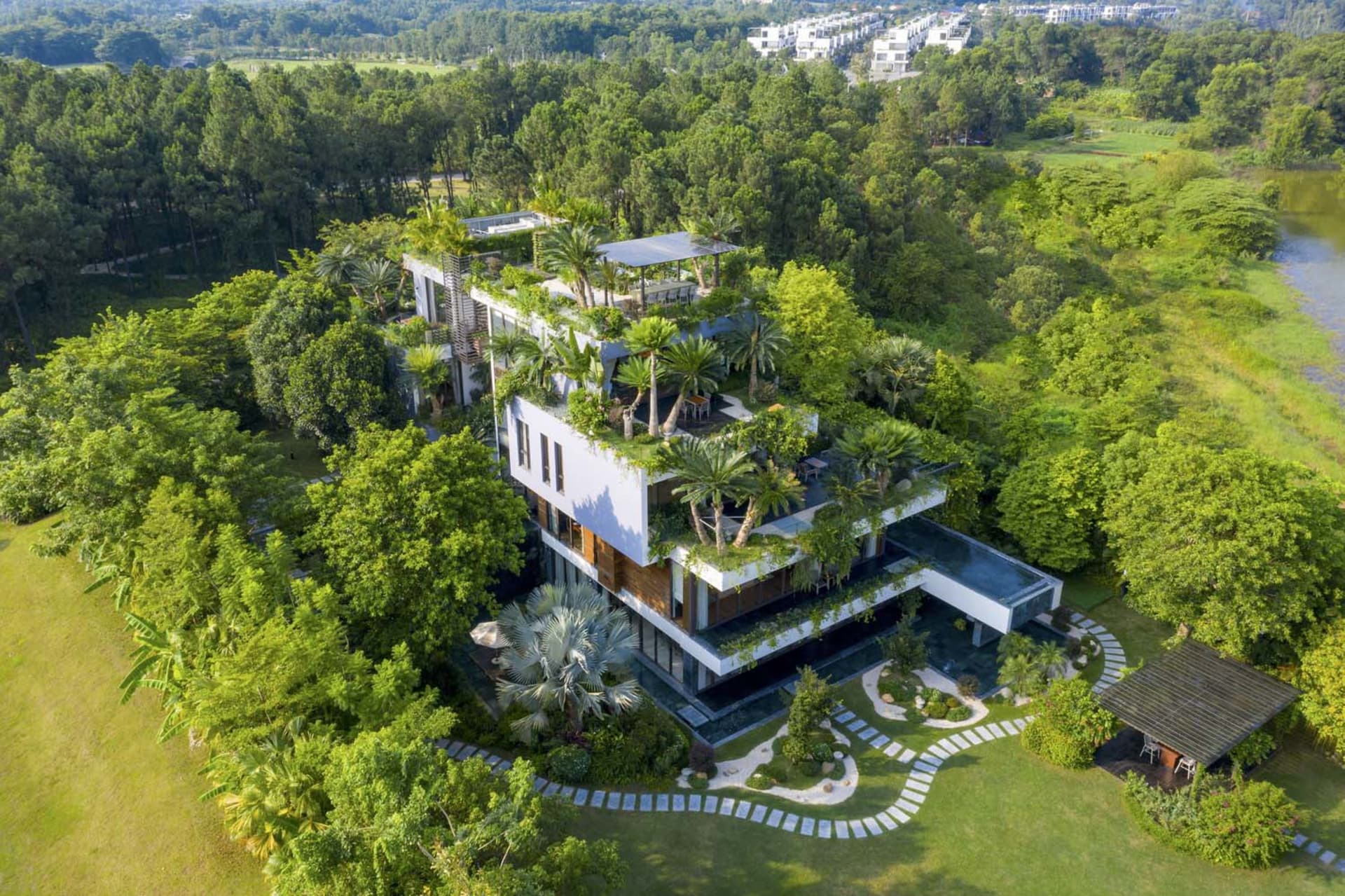 A modern house exterior surrounded by trees and greenery, featuring a metallic roof and outdoor seating areas.