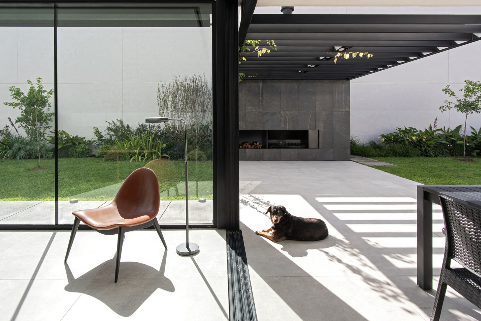 A modern patio with concrete flooring and a brown leather chair, featuring a dog lying on the ground and a grill area.