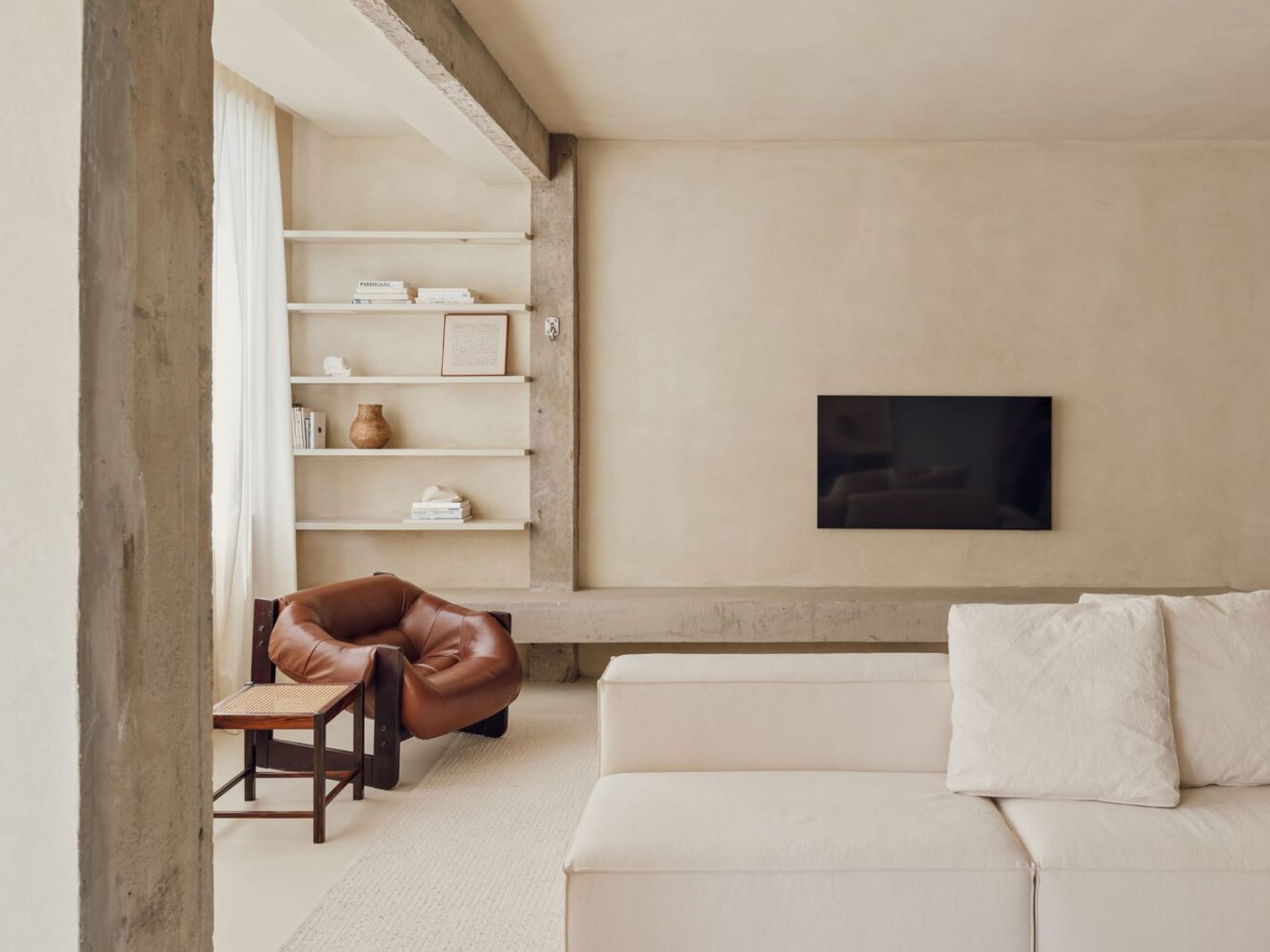 A minimalist living room with concrete shelving, a leather armchair, and a white sofa.