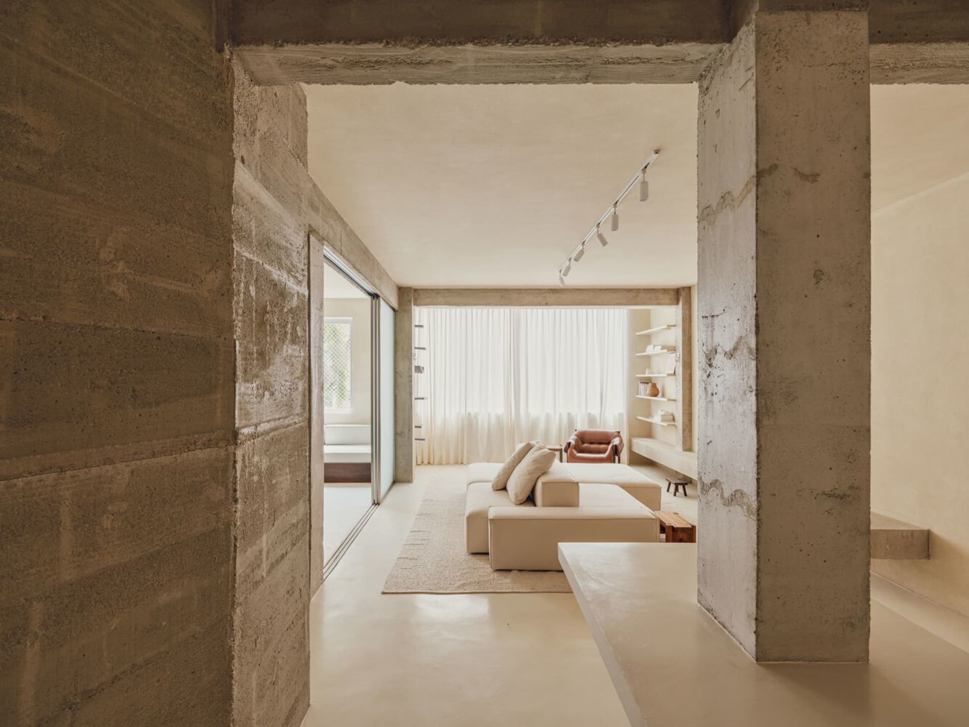 Minimalist living room with concrete walls, white couch, and leather chair.