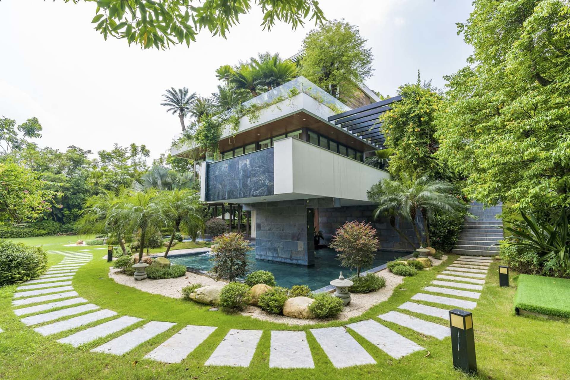 A contemporary residential house with glass walls and stone accents surrounded by lush greenery.