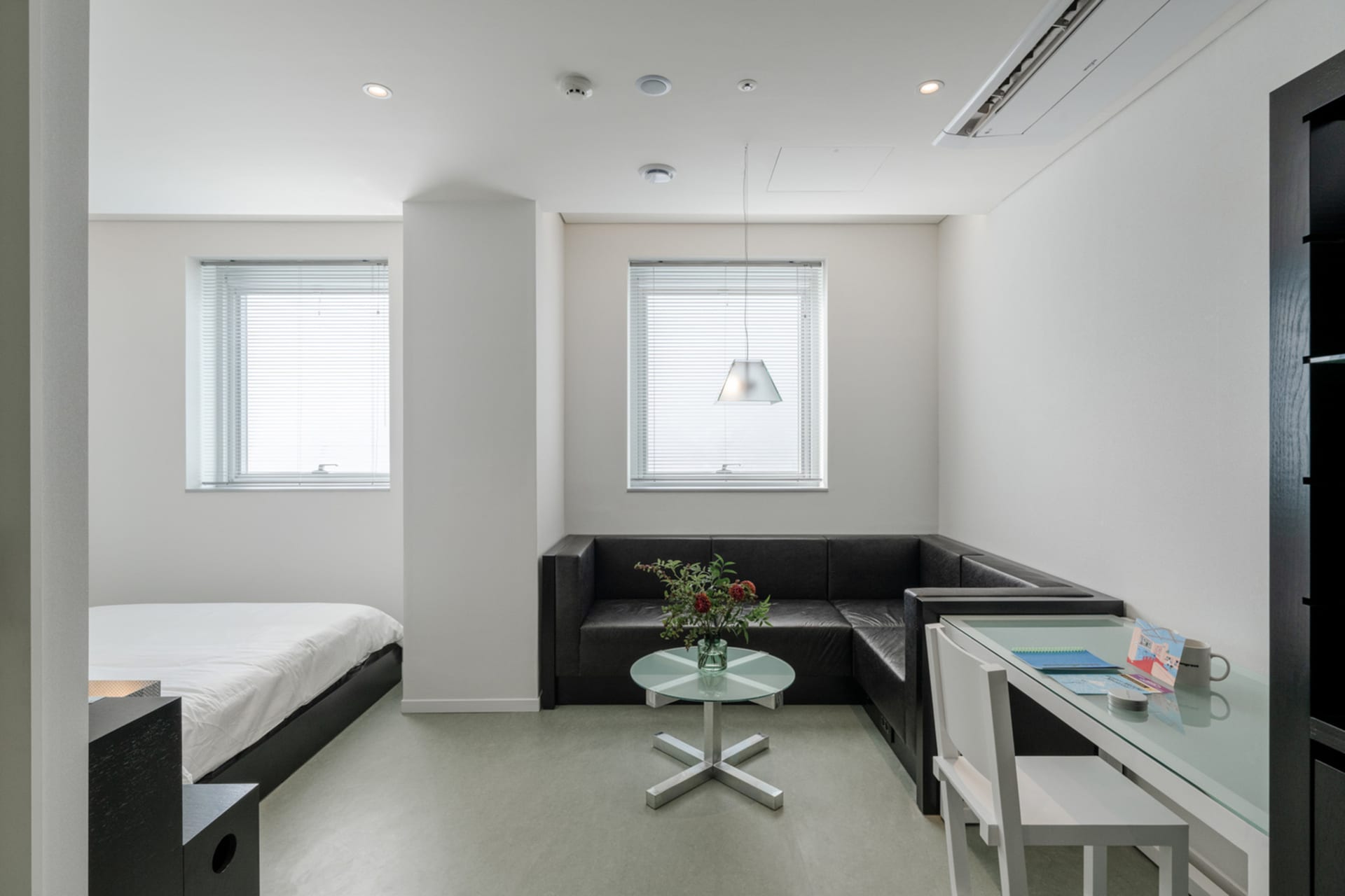 A minimalistic modern studio apartment with metallic accents and a fabric sofa, featuring a glass table and white walls.