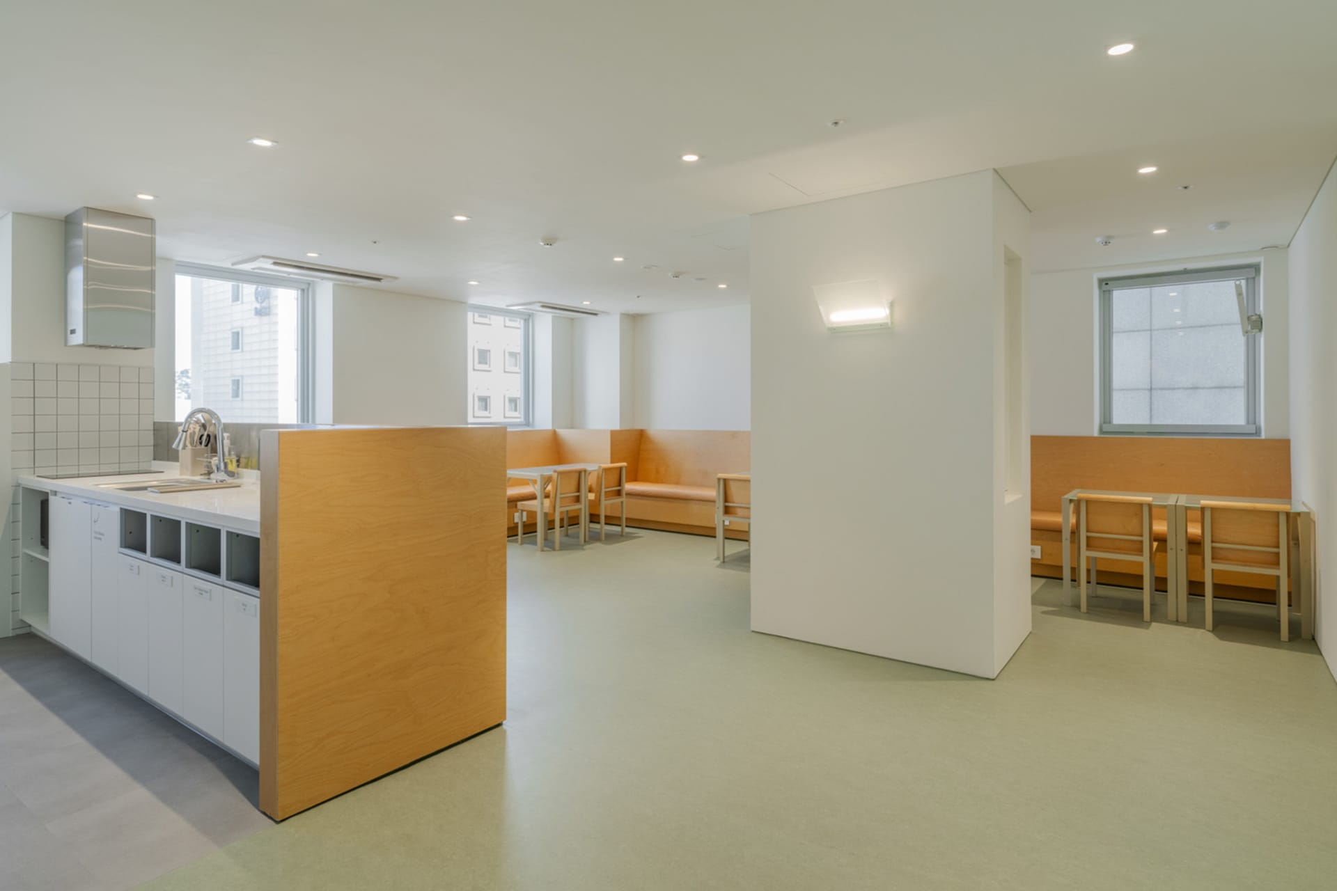 明亮寬敞的社區中心室內,配有木質長椅與桌檯、混凝土地板,以及大型落地窗。