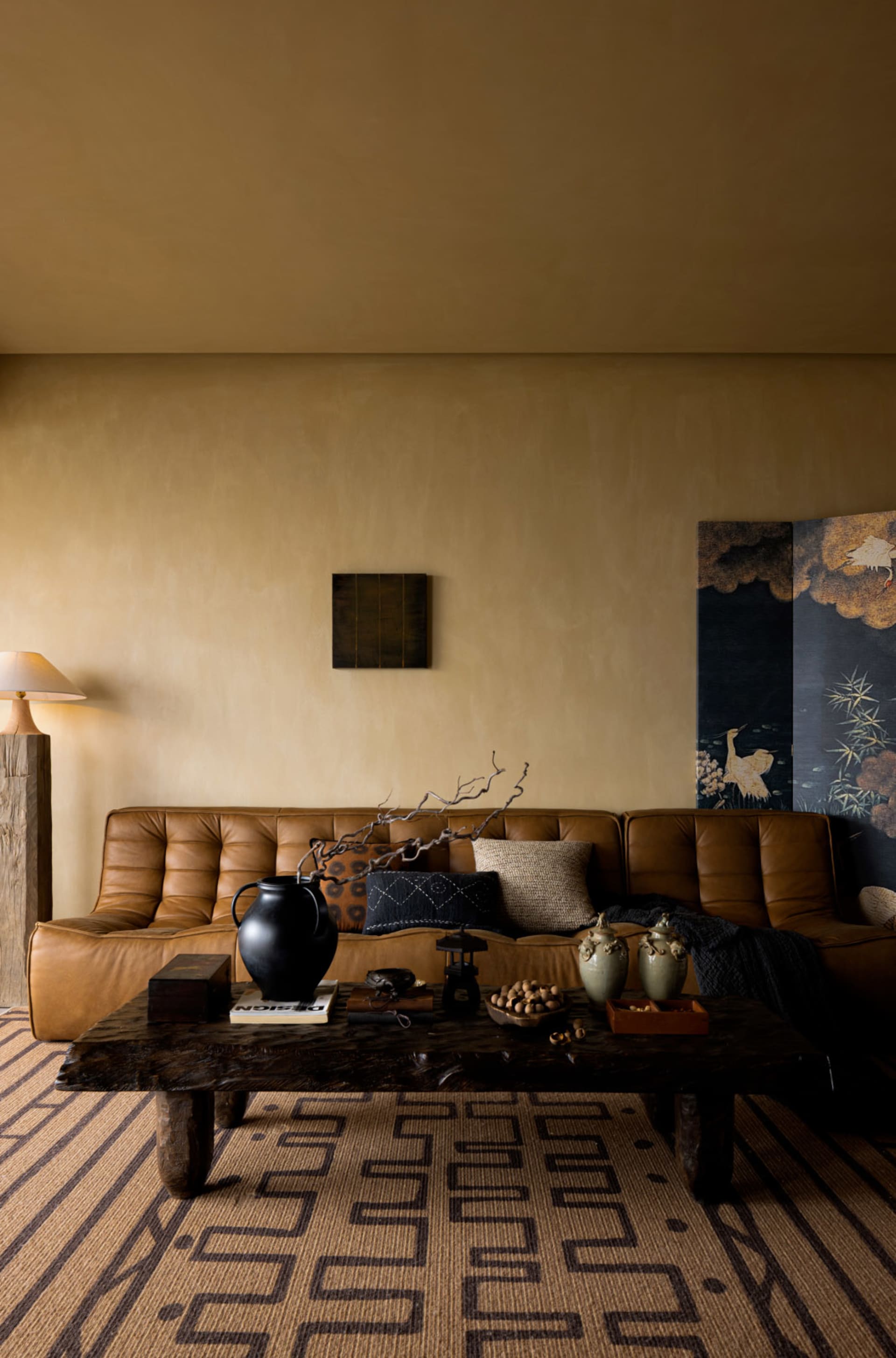 A modern living room featuring a brown leather sofa, a wooden table with decorative items, and a floor lamp in the corner.