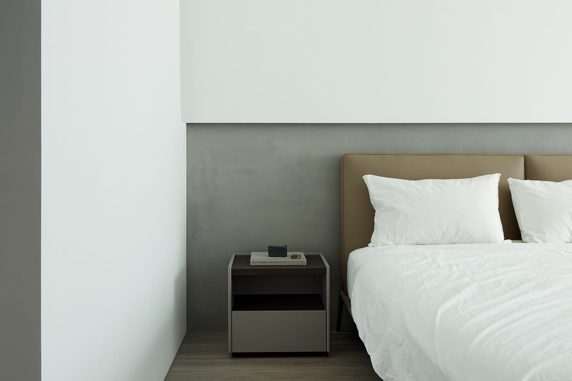 A modern minimalist bedroom featuring a concrete headboard and white bedding.