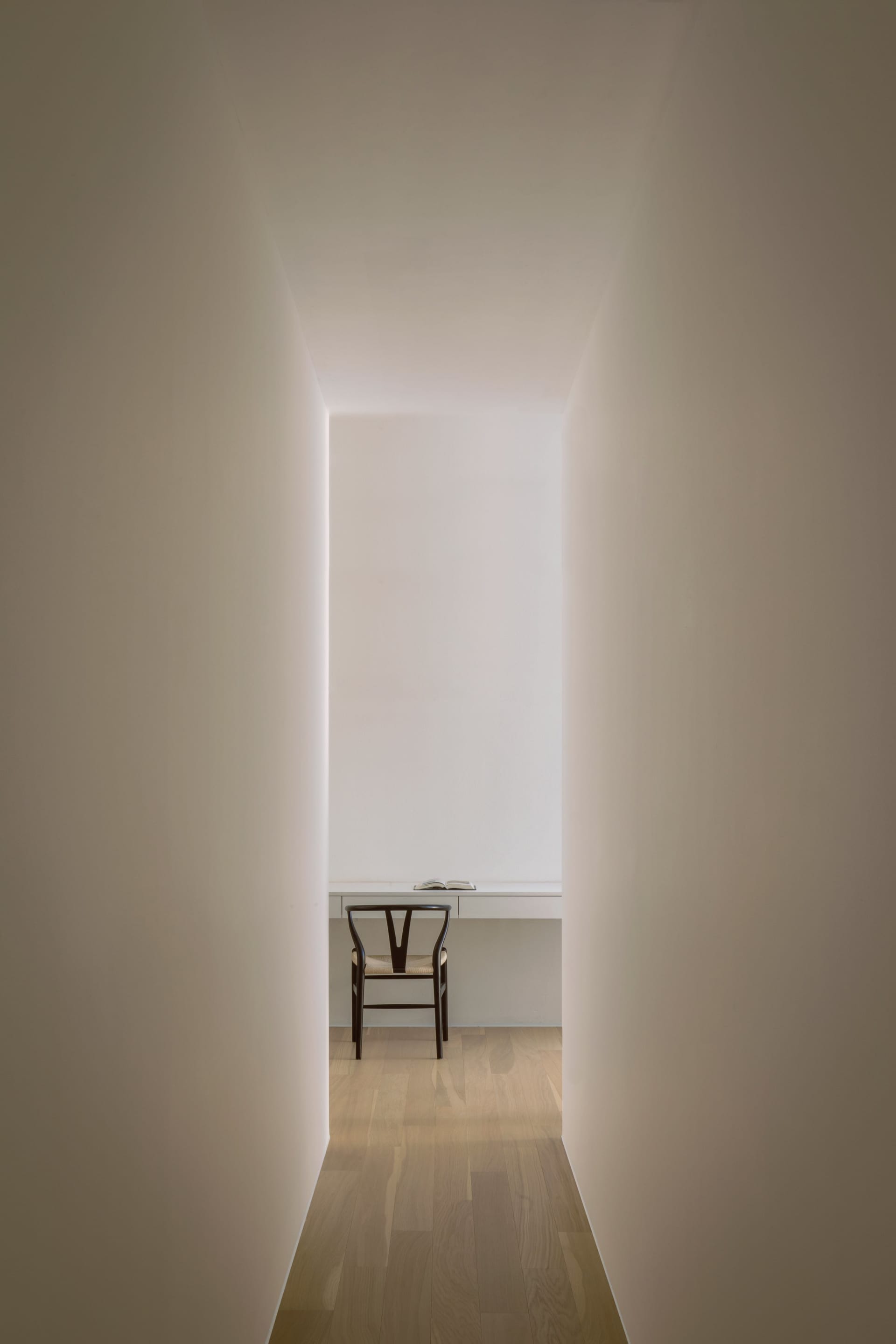 A minimalist workspace with a black chair and wooden desk in a corridor with illuminated walls.