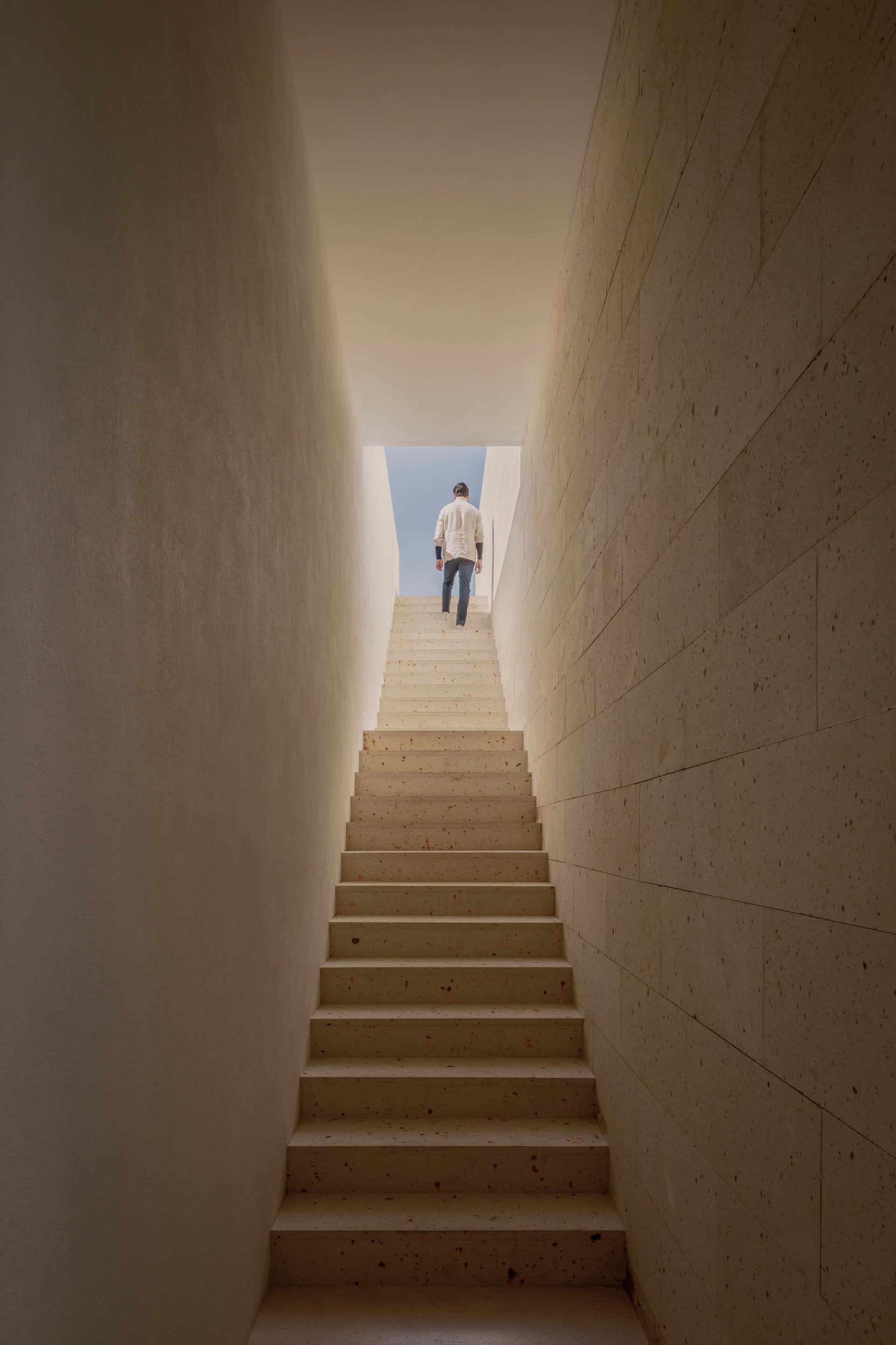 A man walking down a concrete staircase leading to a bright, open sky.