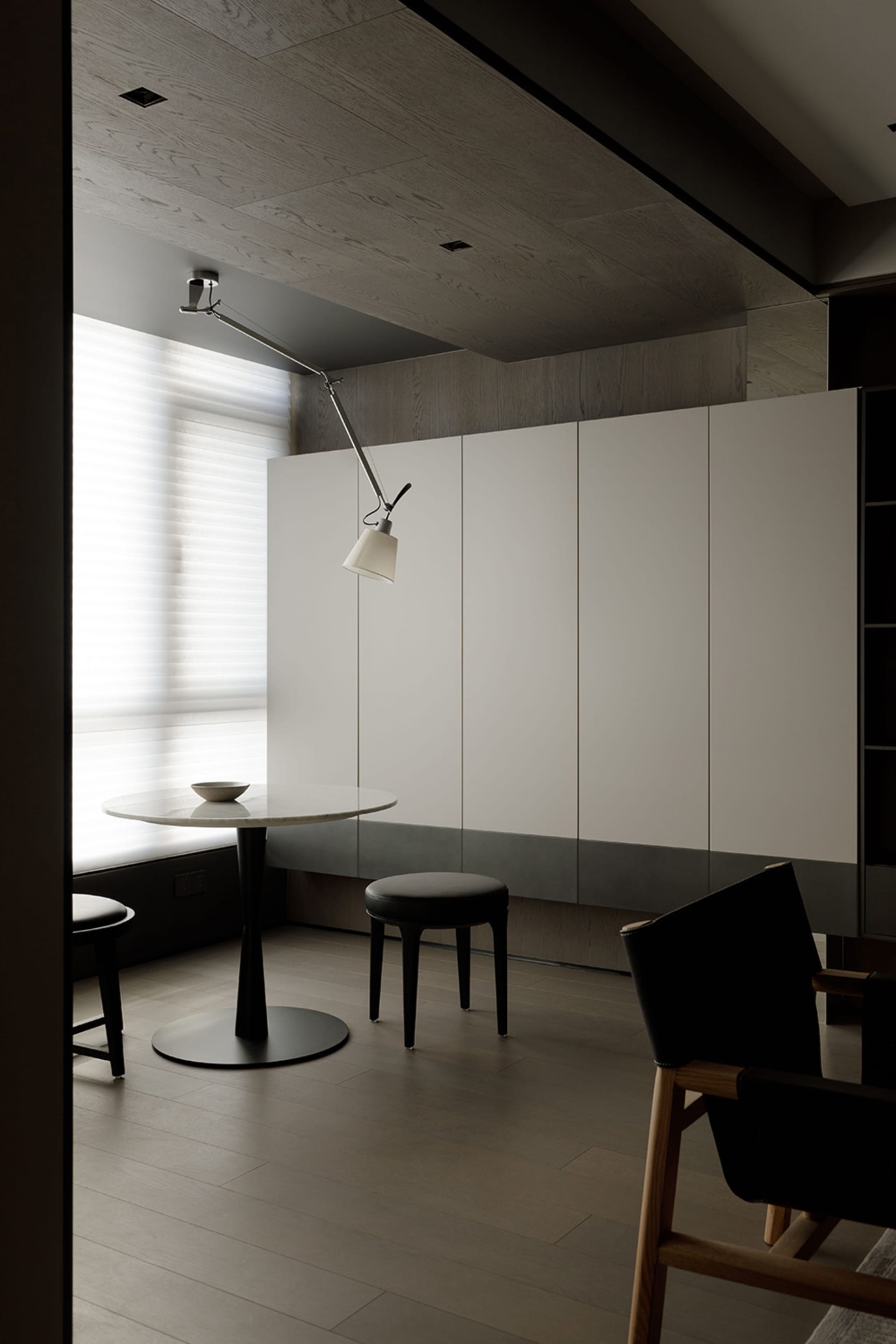 A modern kitchen featuring a white marble table with black legs, a black stool, and a minimalist design with white cabinets.