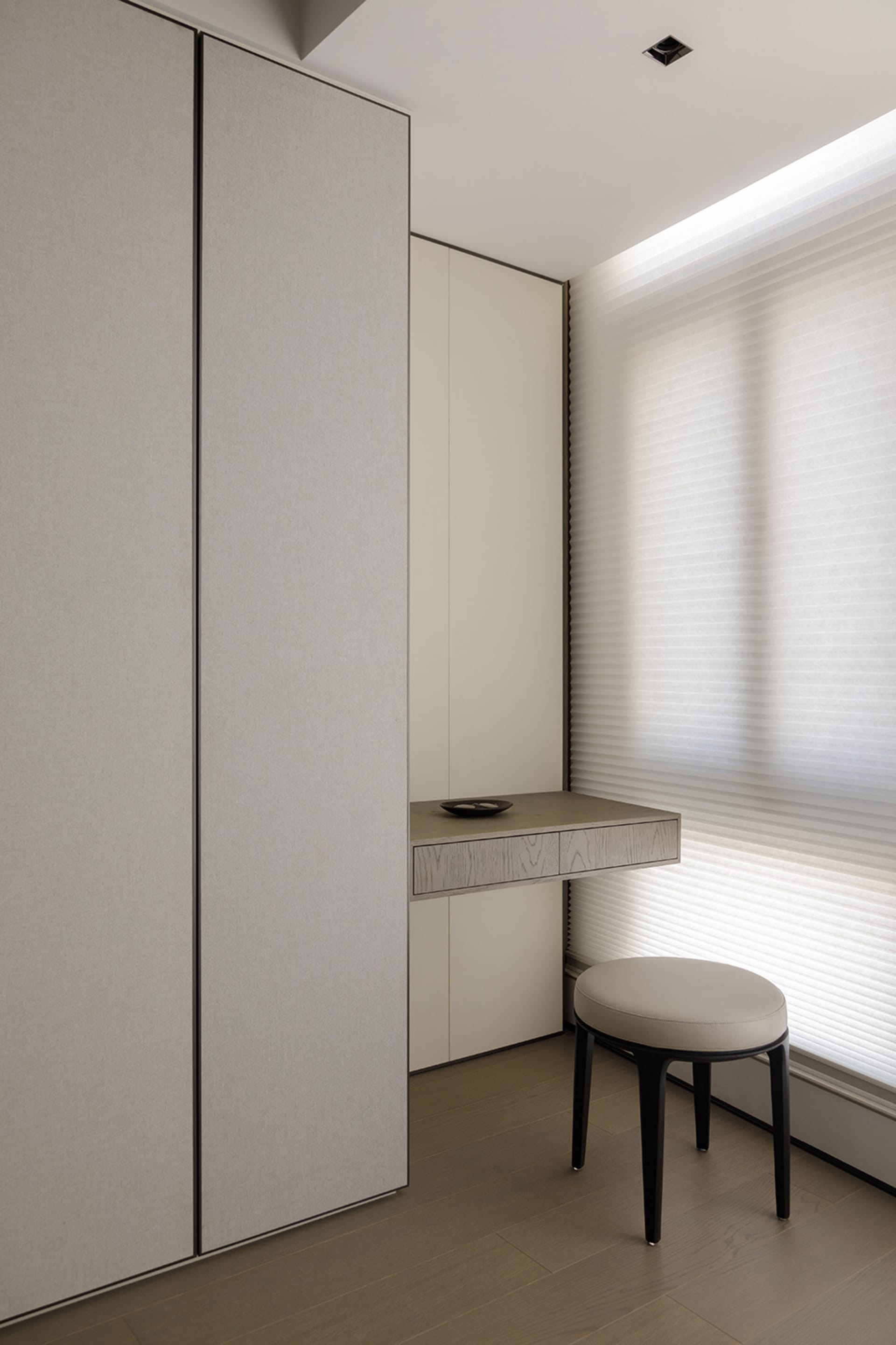 A minimalist study space featuring neutral-colored furniture and a window with sheer blinds.
