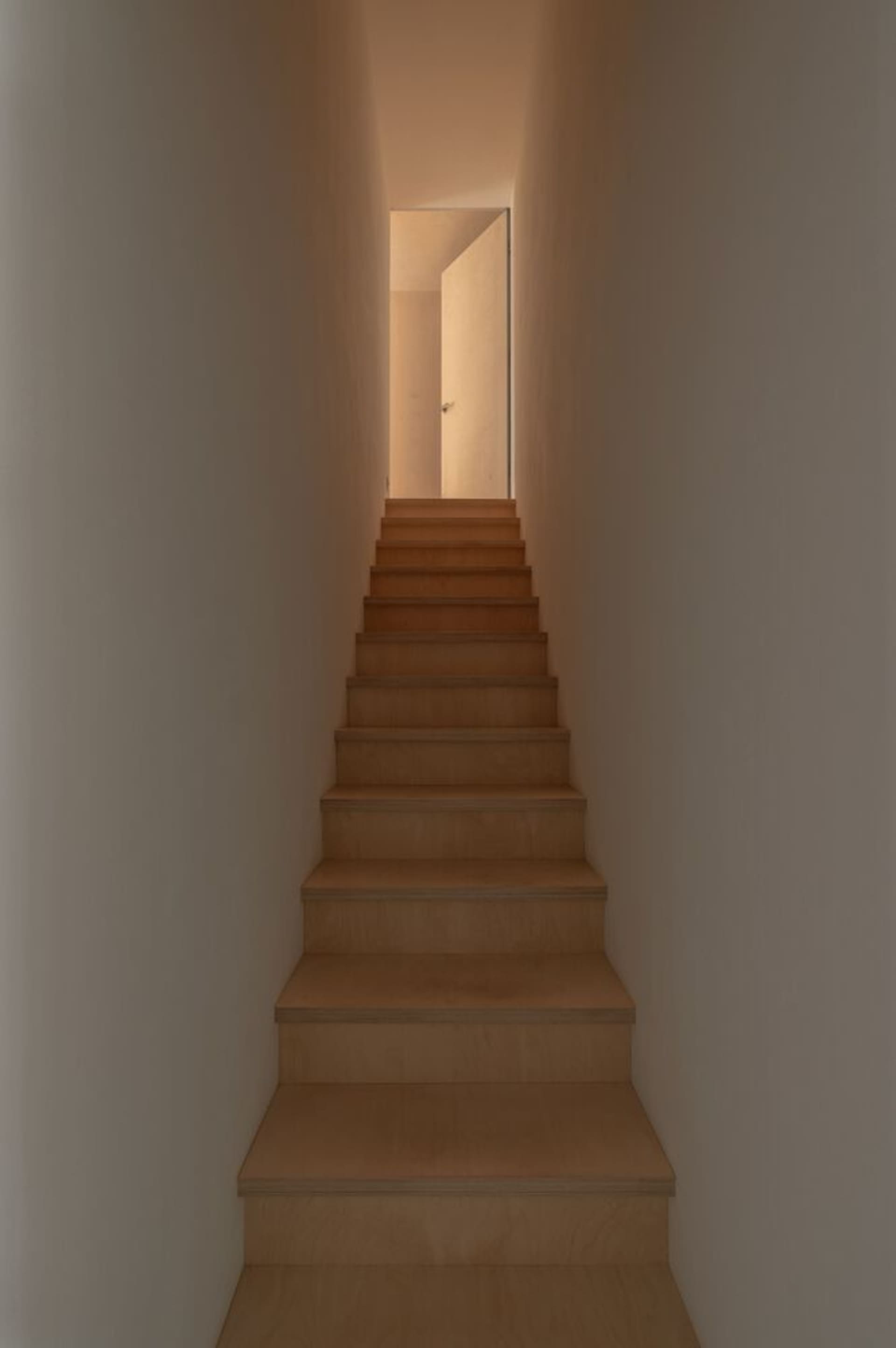 A minimalist staircase made of wood with a warm light at the end.