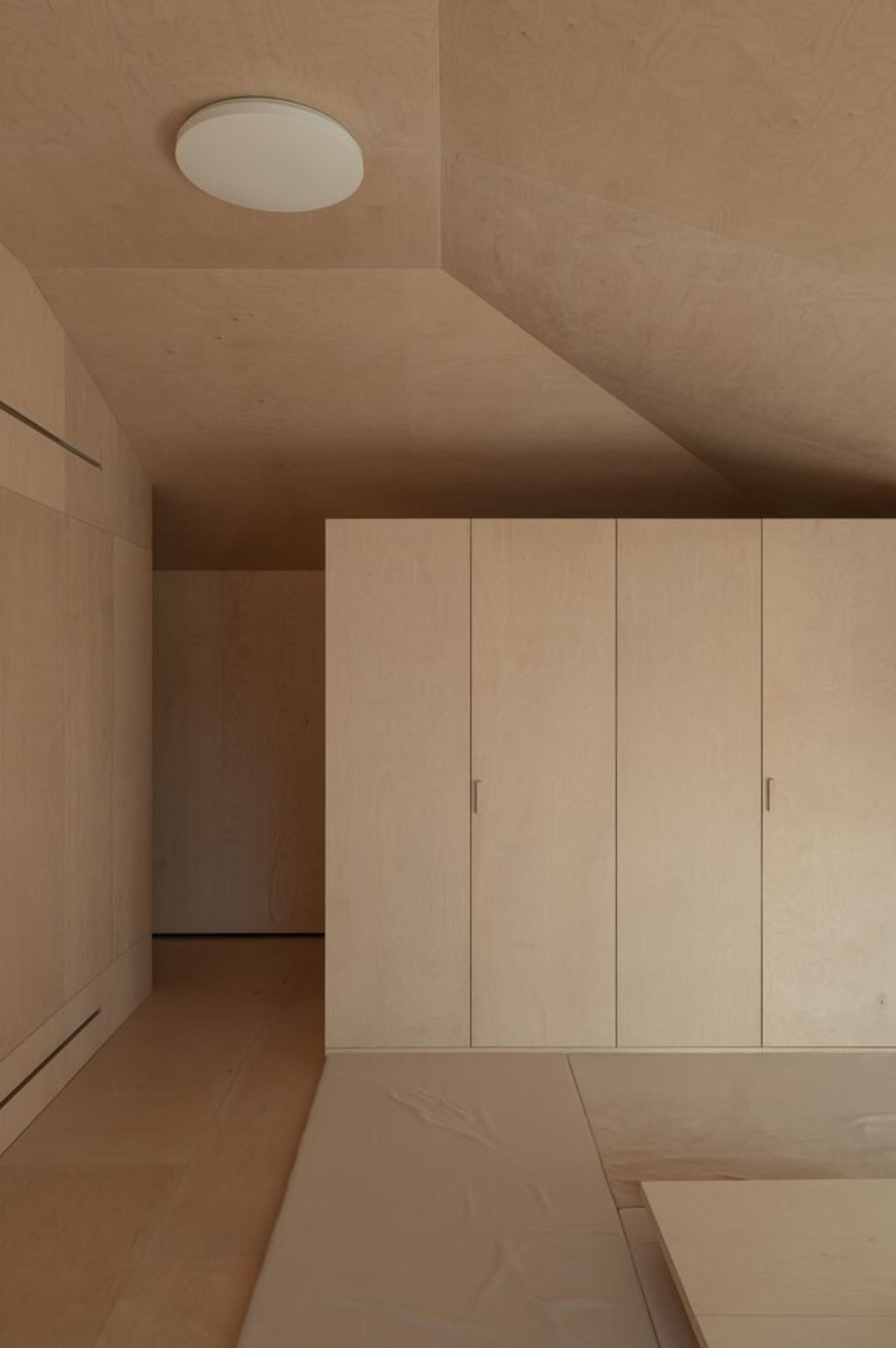 A minimalist room with wall closets made of birch plywood.