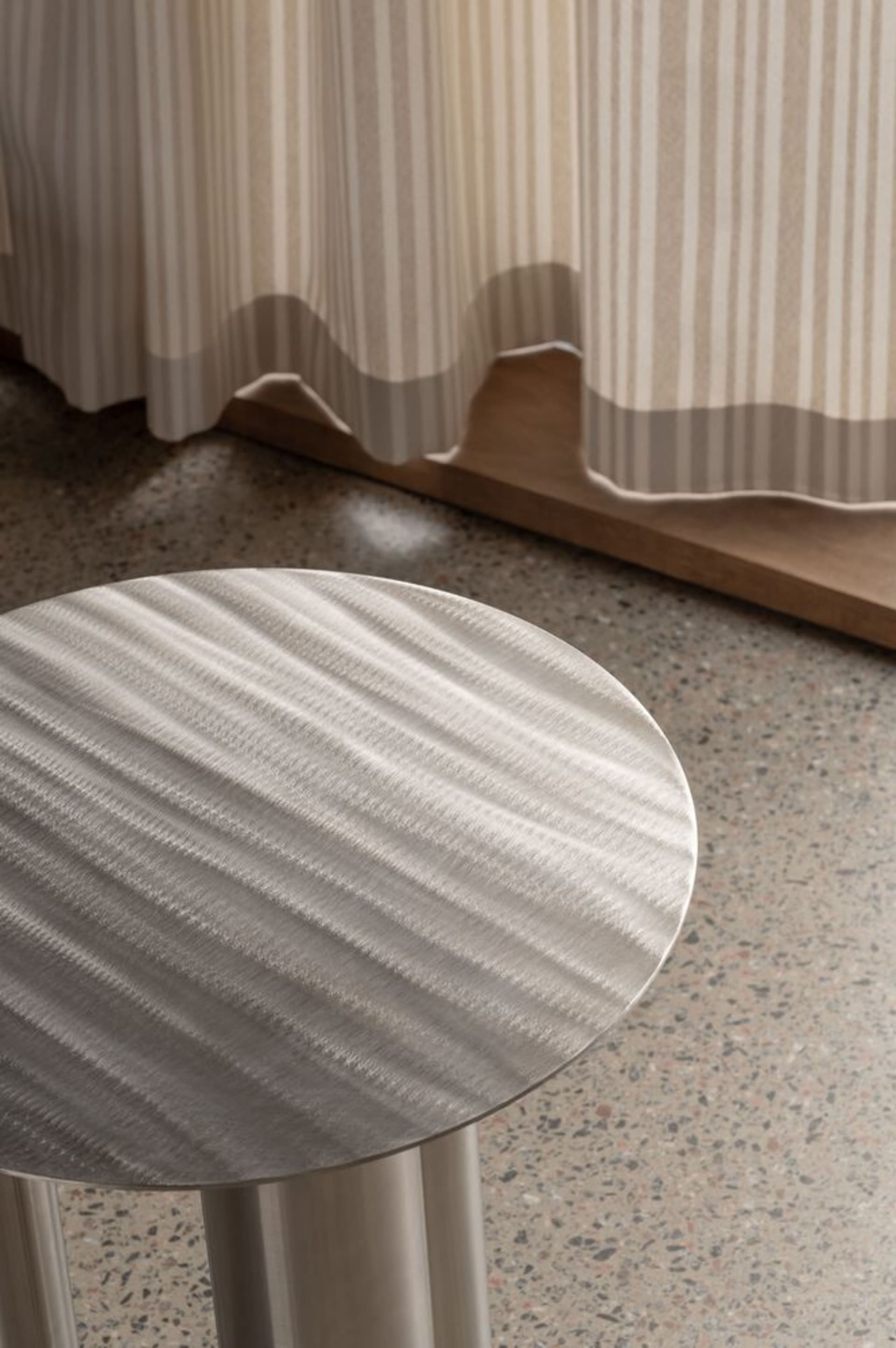 Modern metal side table with a textured surface in a contemporary interior setting.