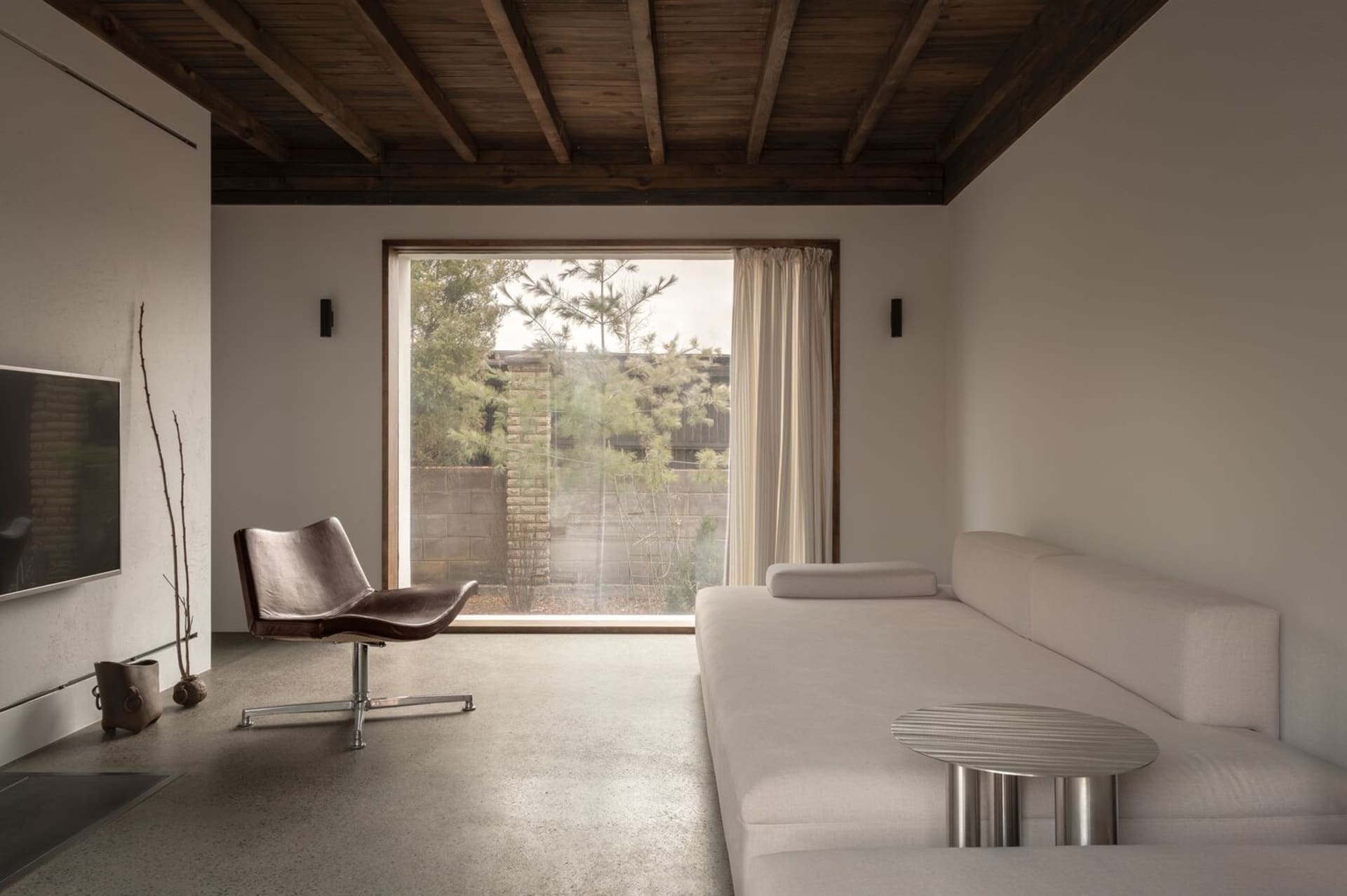 Modern living room with concrete floor, leather armchair, and upholstered sofa.
