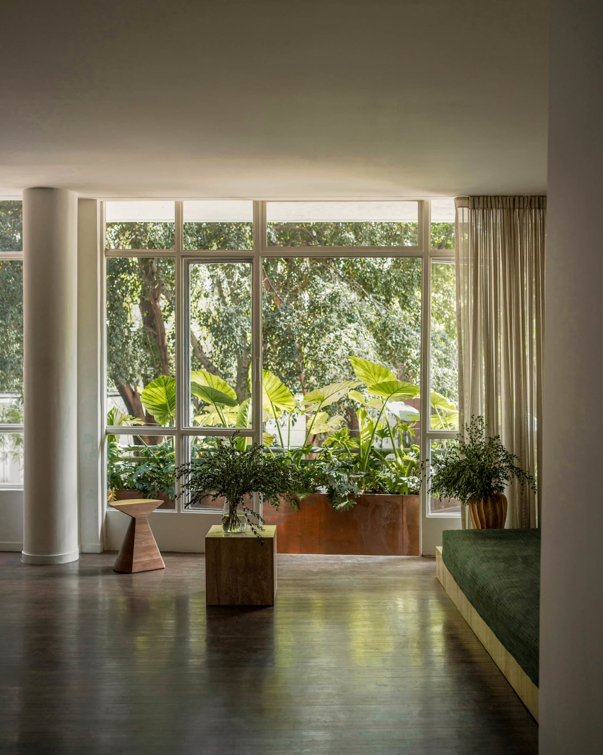 A modern industrial living room interior with concrete walls and floor, large windows, and green plants.