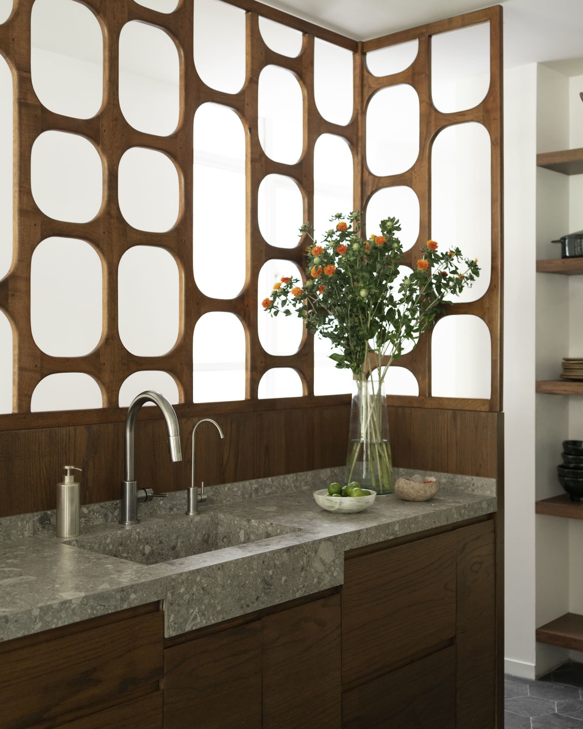 A modern kitchen with a marble countertop featuring a sink, faucet, and decorative items like a vase of flowers and a bowl of
