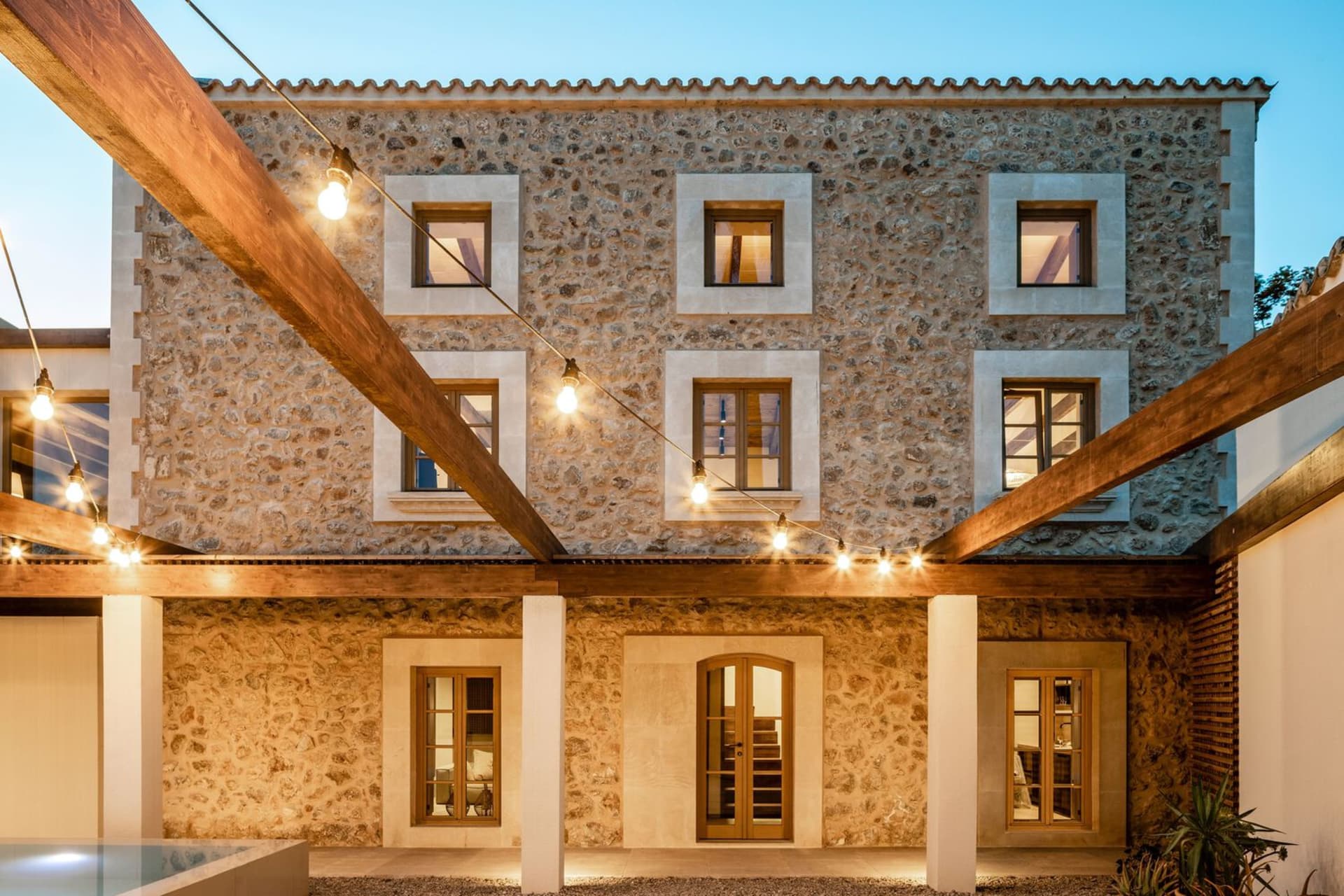 Stone exterior of a house at night with lights strung overhead.