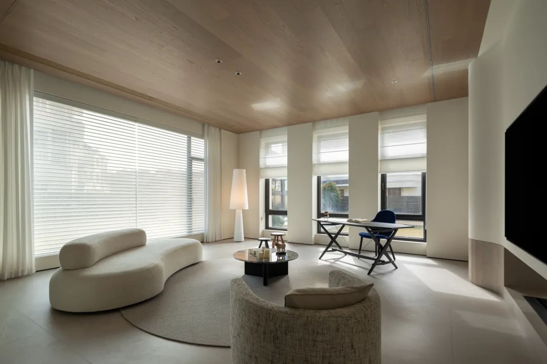 Modern minimalist living room with white furniture, wooden ceiling, and large windows showcasing a clean and bright interior