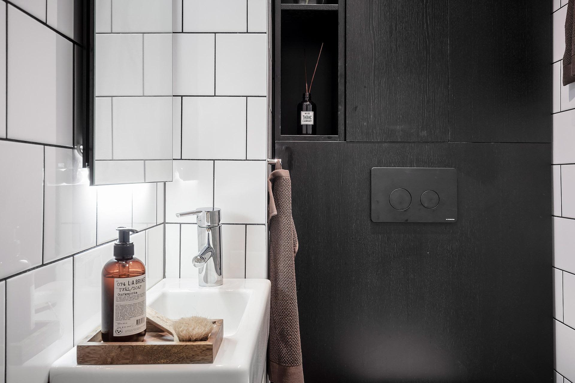Modern minimalist bathroom with black and white ceramics, black wooden cabinets, and metallic bathroom fixtures.