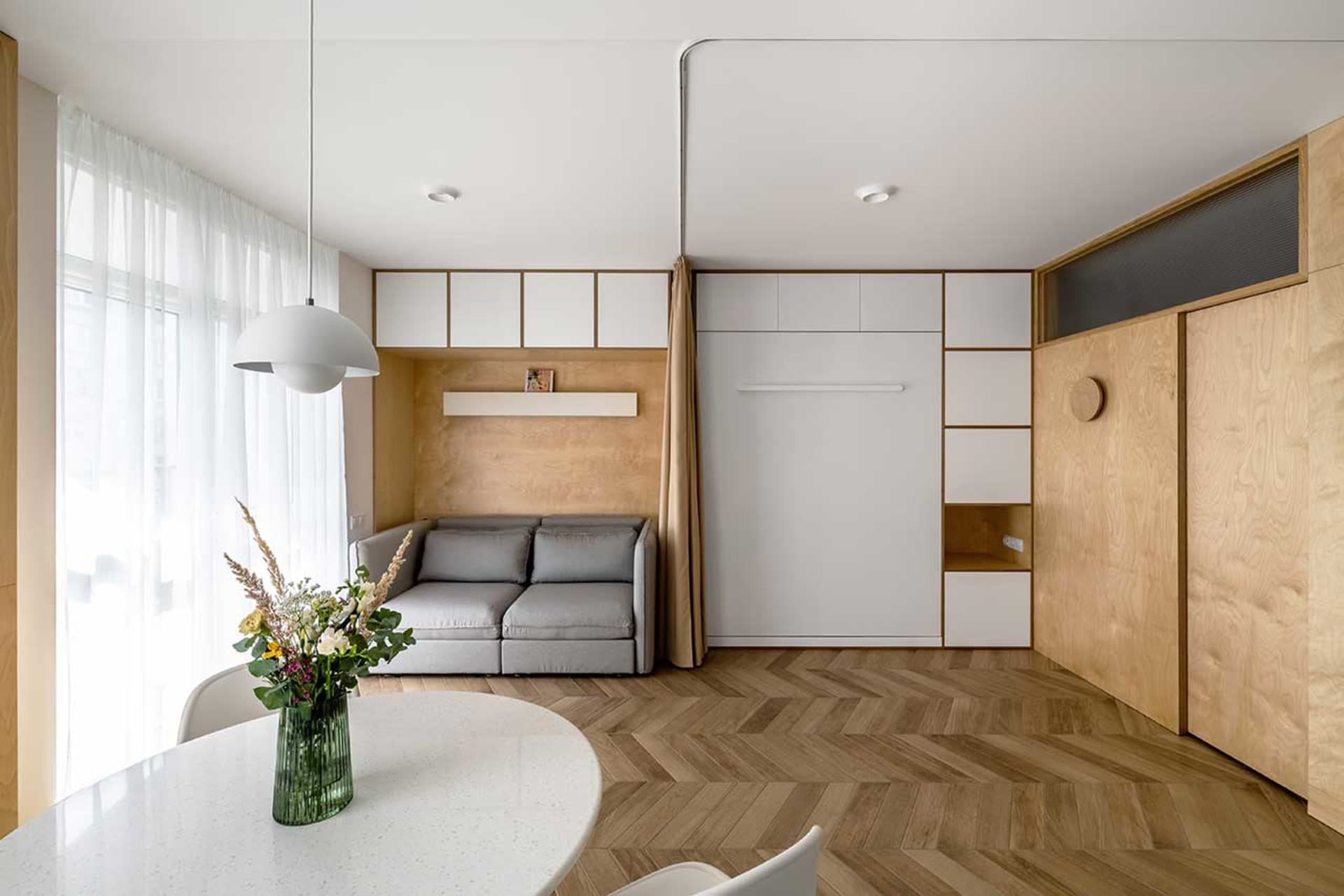 A modern apartment with minimalist design featuring wooden furniture and white walls and cabinets.