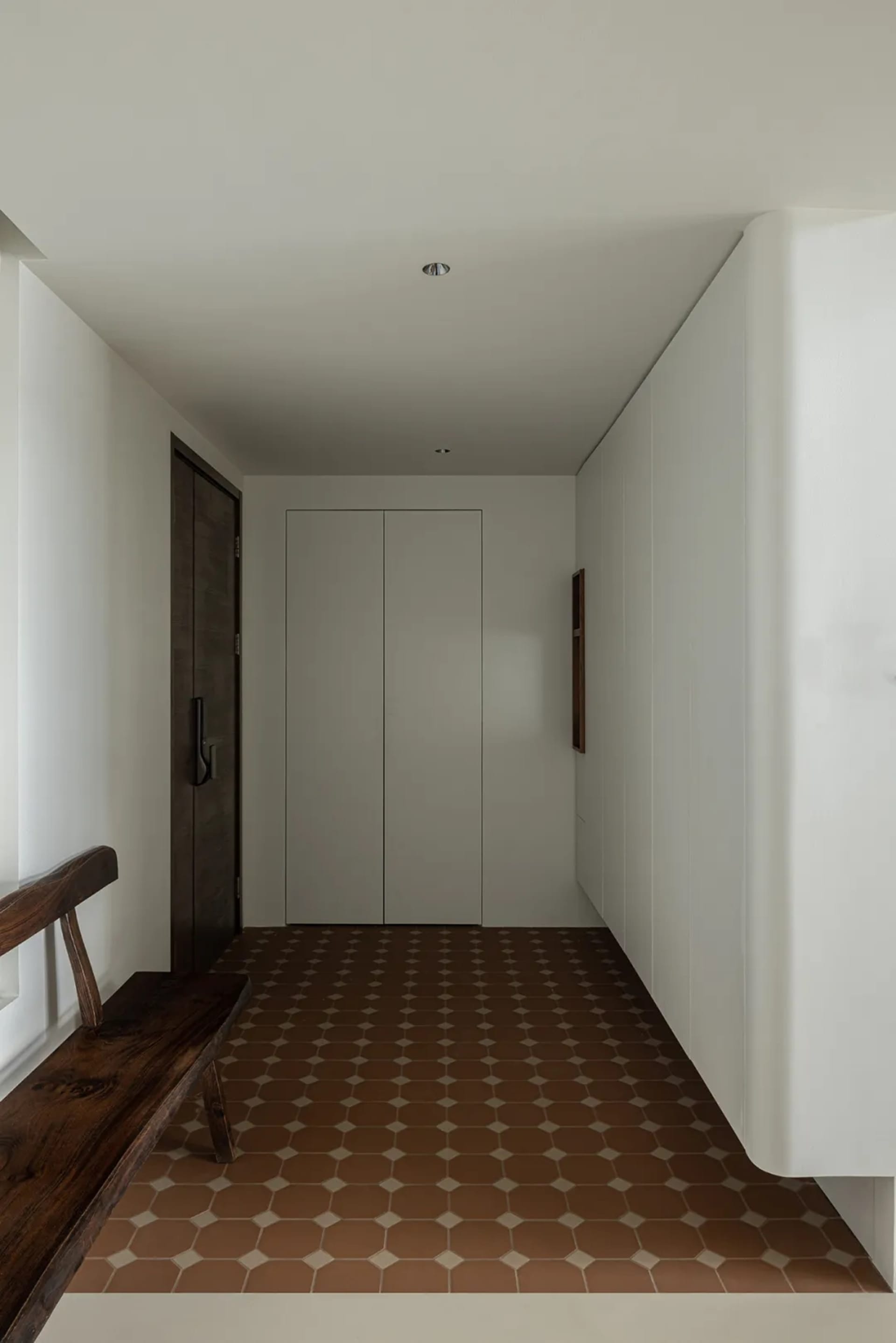A minimalist entryway featuring a tiled floor and wooden bench against white walls.