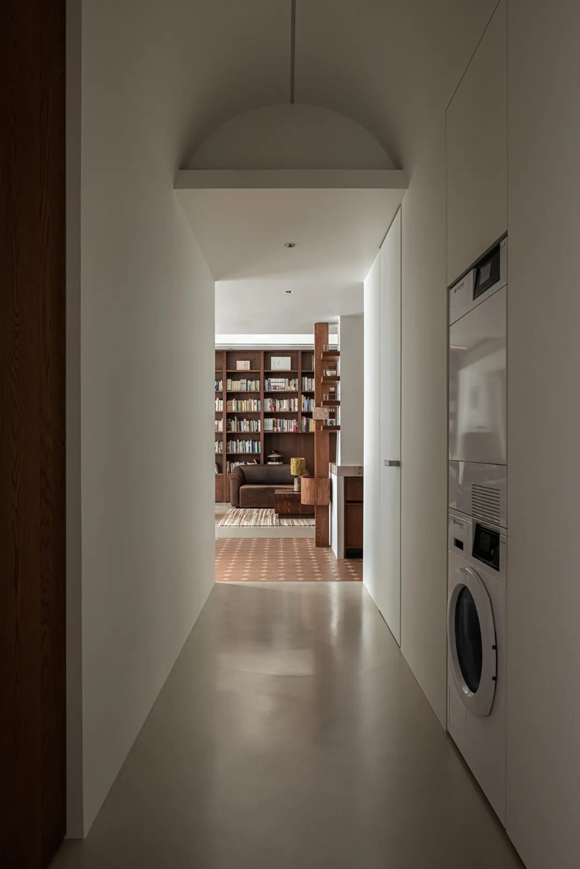 A modern contemporary living room with concrete flooring and a large bookshelf filled with books.