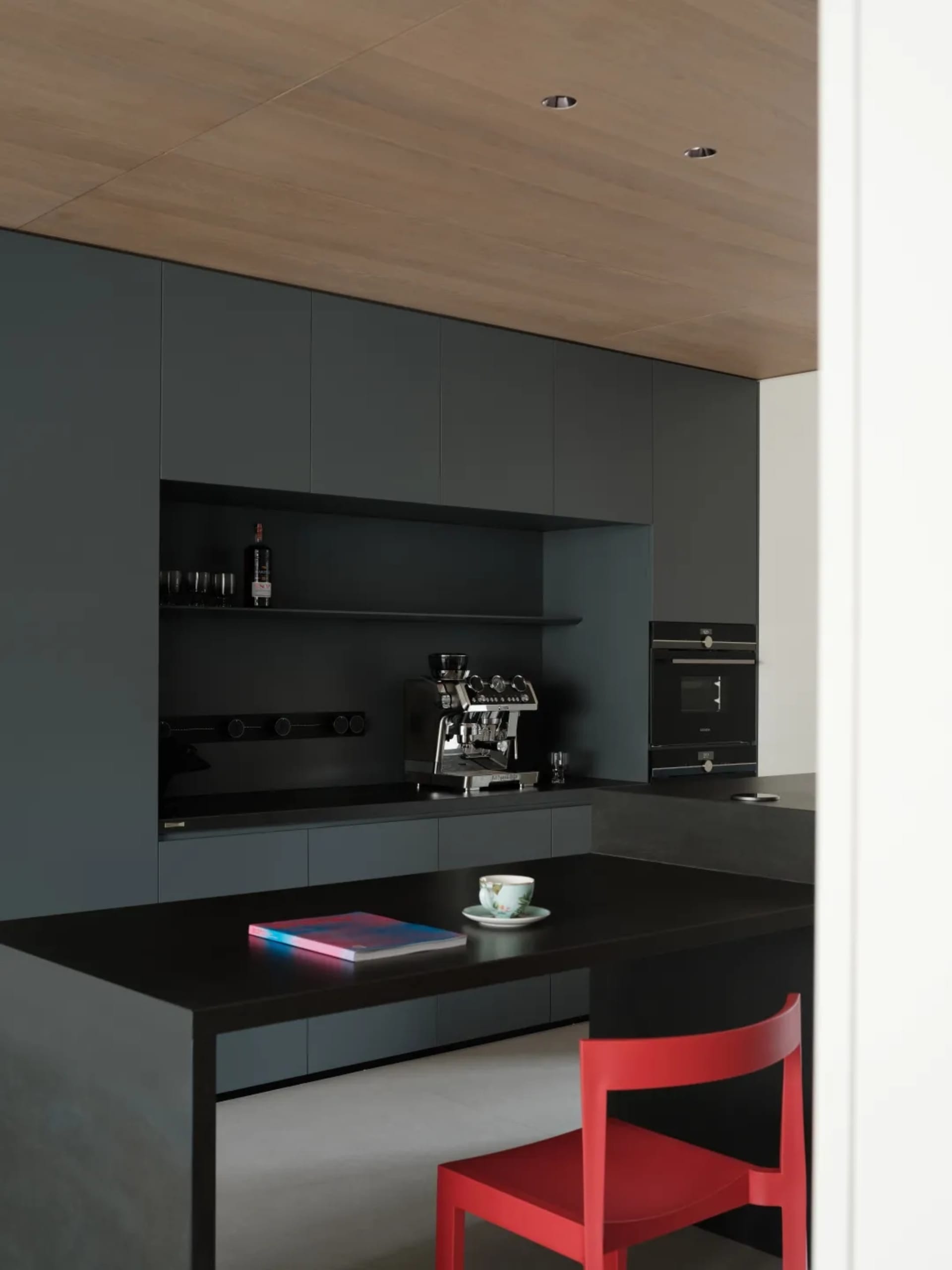 A modern kitchen featuring sleek black steel cabinets, a countertop espresso machine, and a red chair.