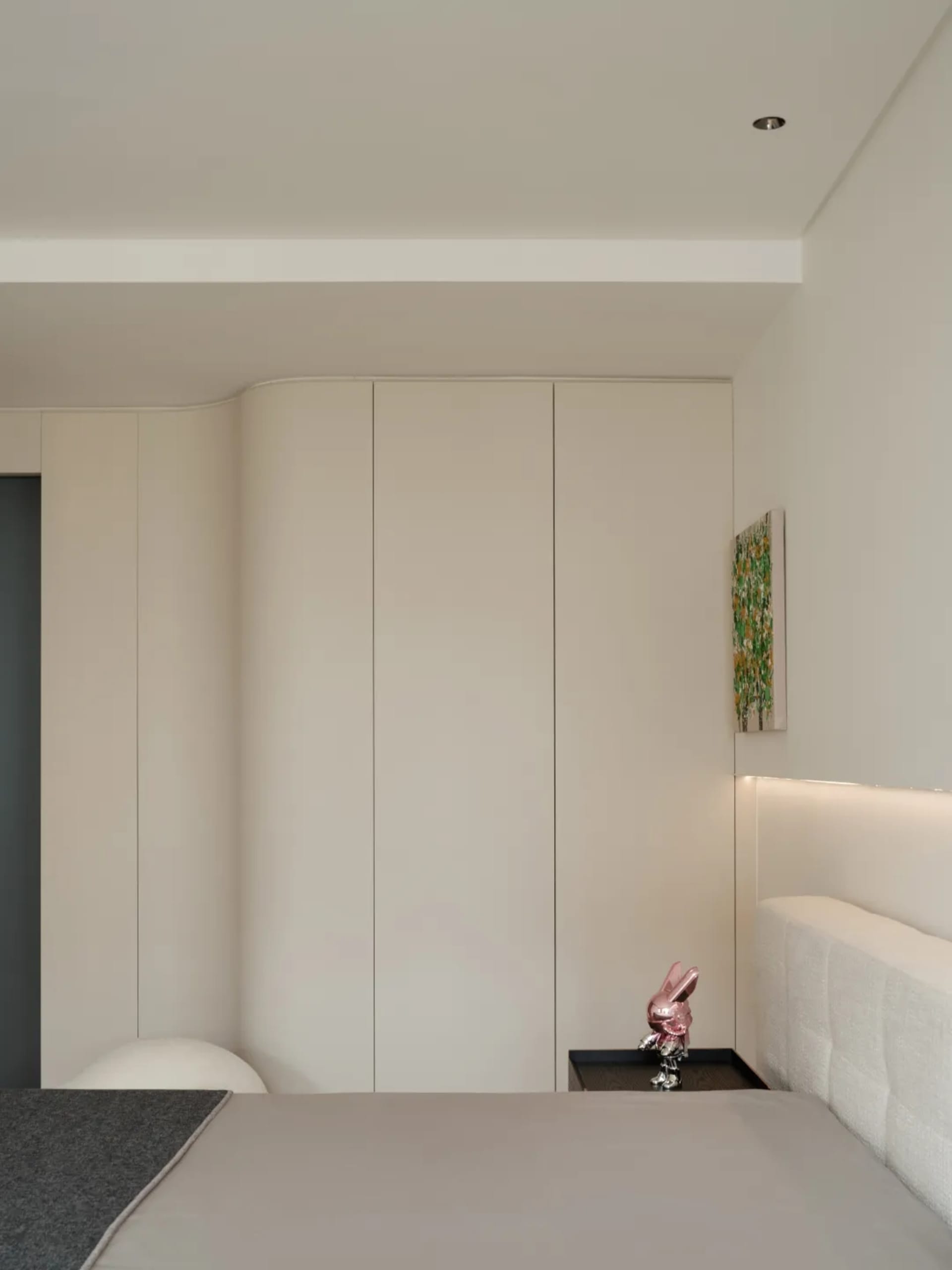 A minimalist bedroom with white furniture and a large window, featuring a bed and a white headboard.