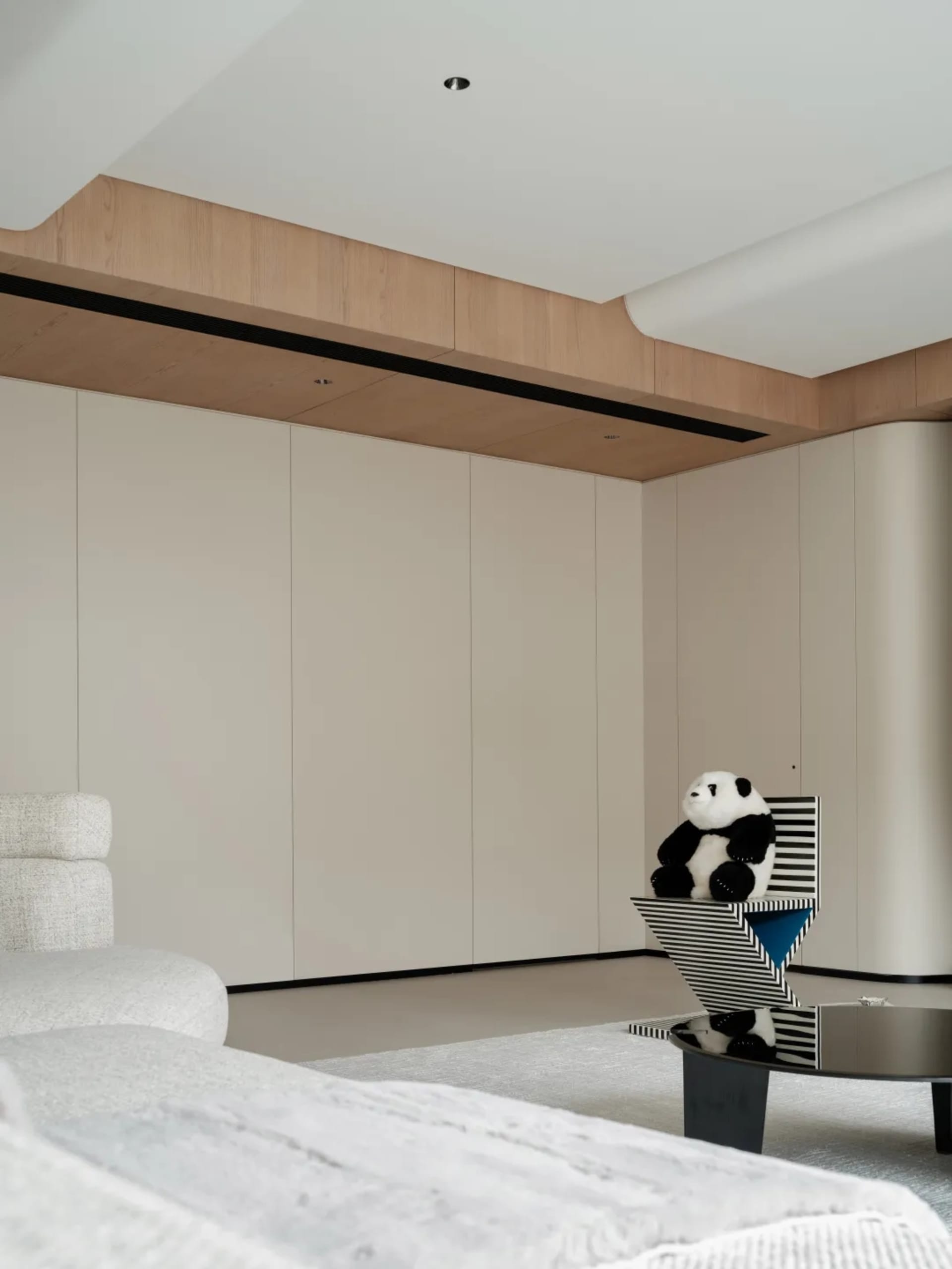 A modern minimalist bedroom with white cabinets, a white upholstered bed, and a white panda stuffed toy on a geometrically de