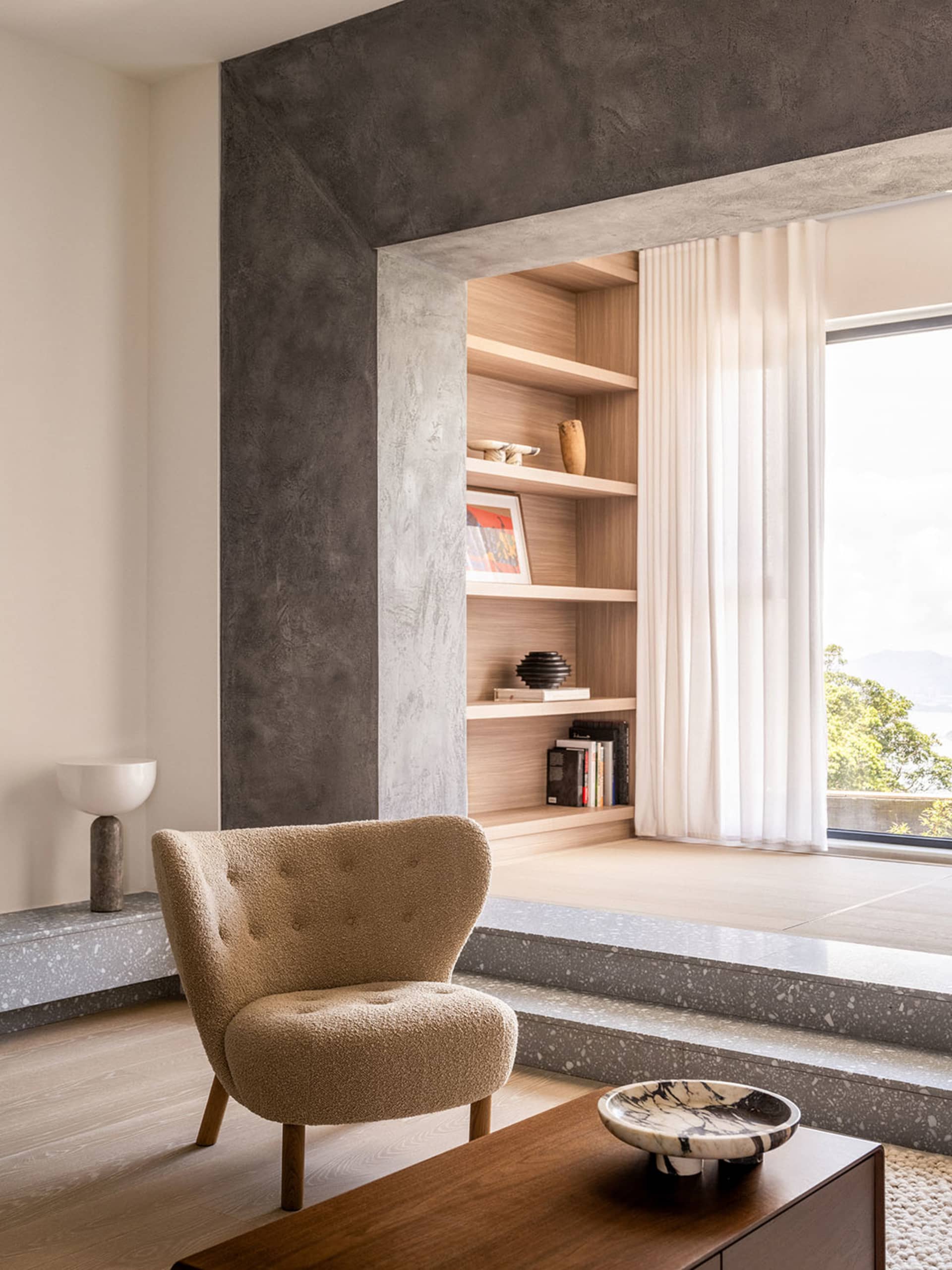 A minimalist living room with a terrazzo floor, curtains, and a bookshelf.
