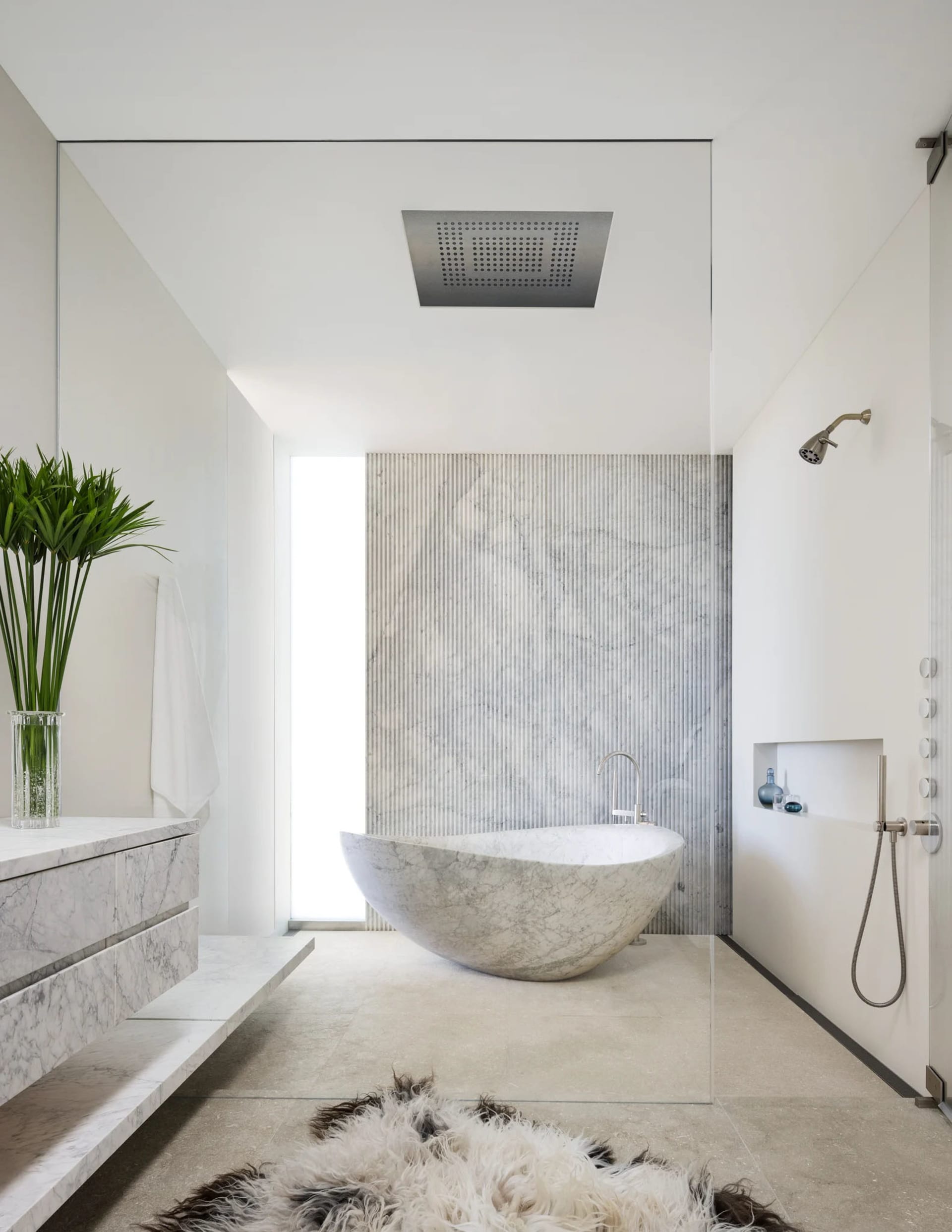 Modern minimalist bathroom with a freestanding marble tub, white walls, and a white marble pedestal sink.