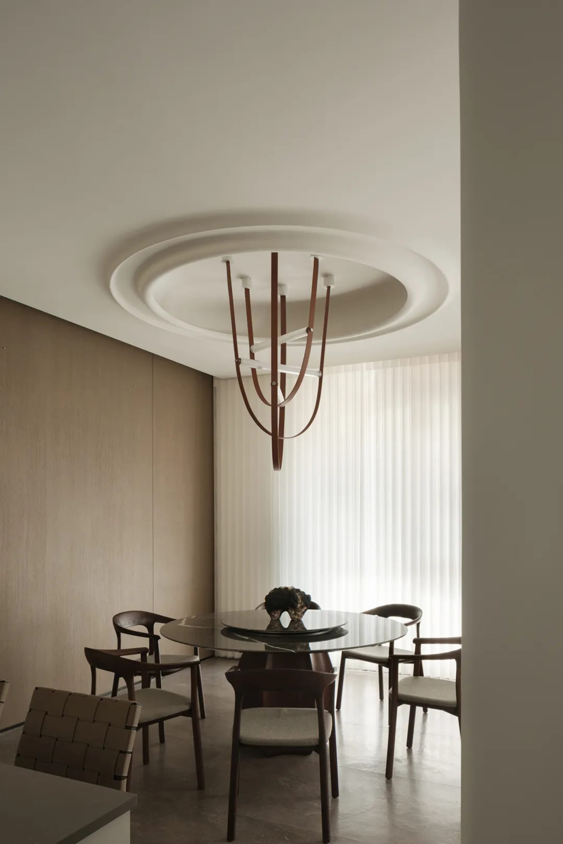 A minimalist dining room with a round glass table, wooden chairs, and a modern chandelier.