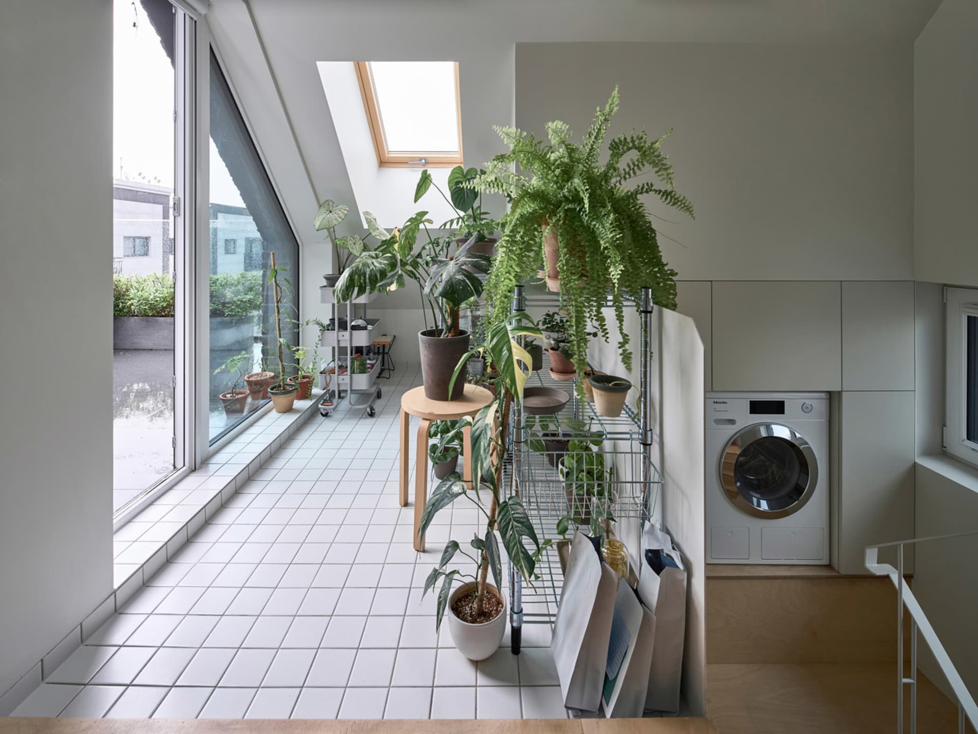 A modern industrial laundry room with white tiles, metal shelves, and various potted plants.