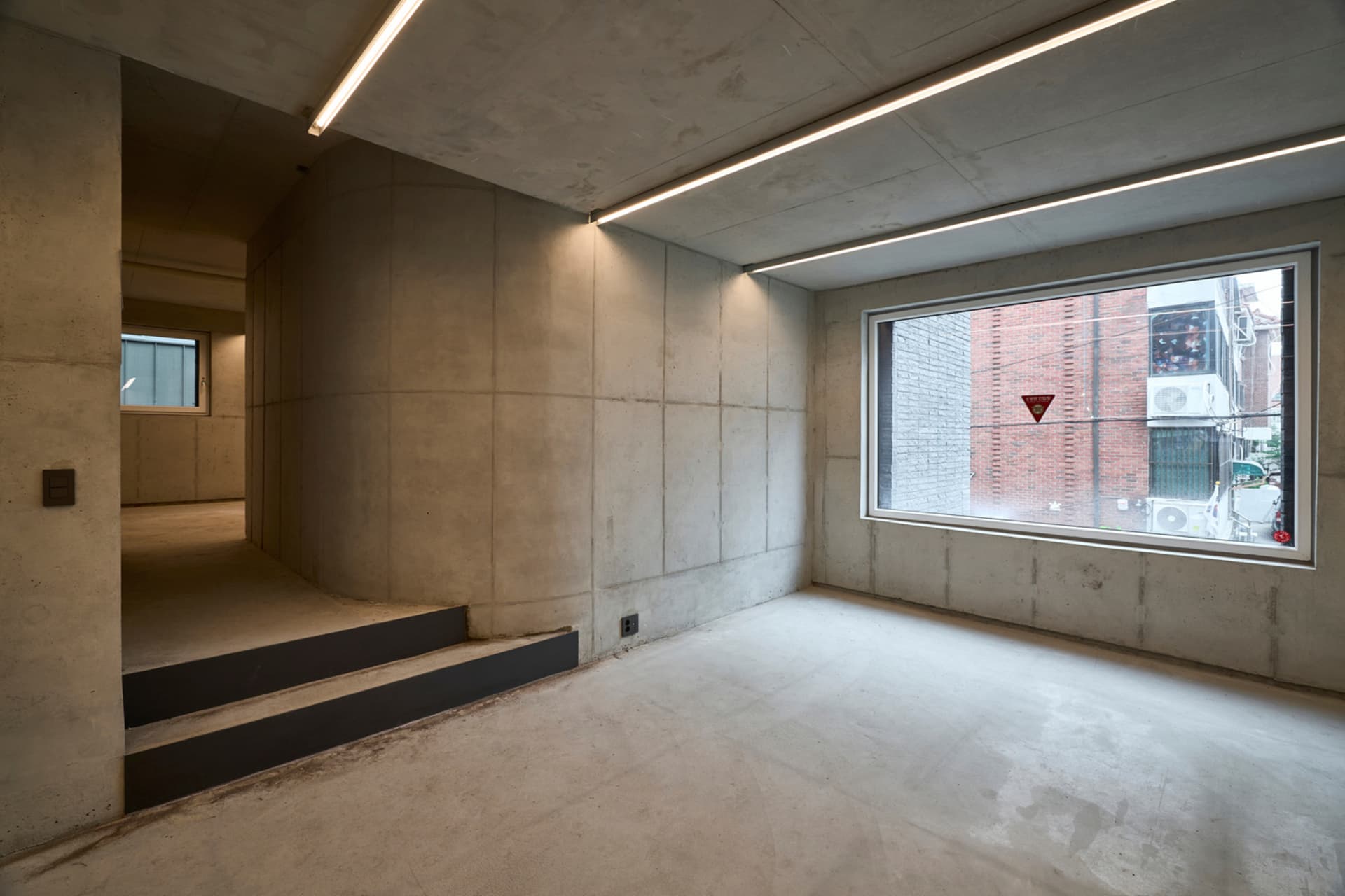 A spacious, minimalist industrial-style room with concrete walls and floors.