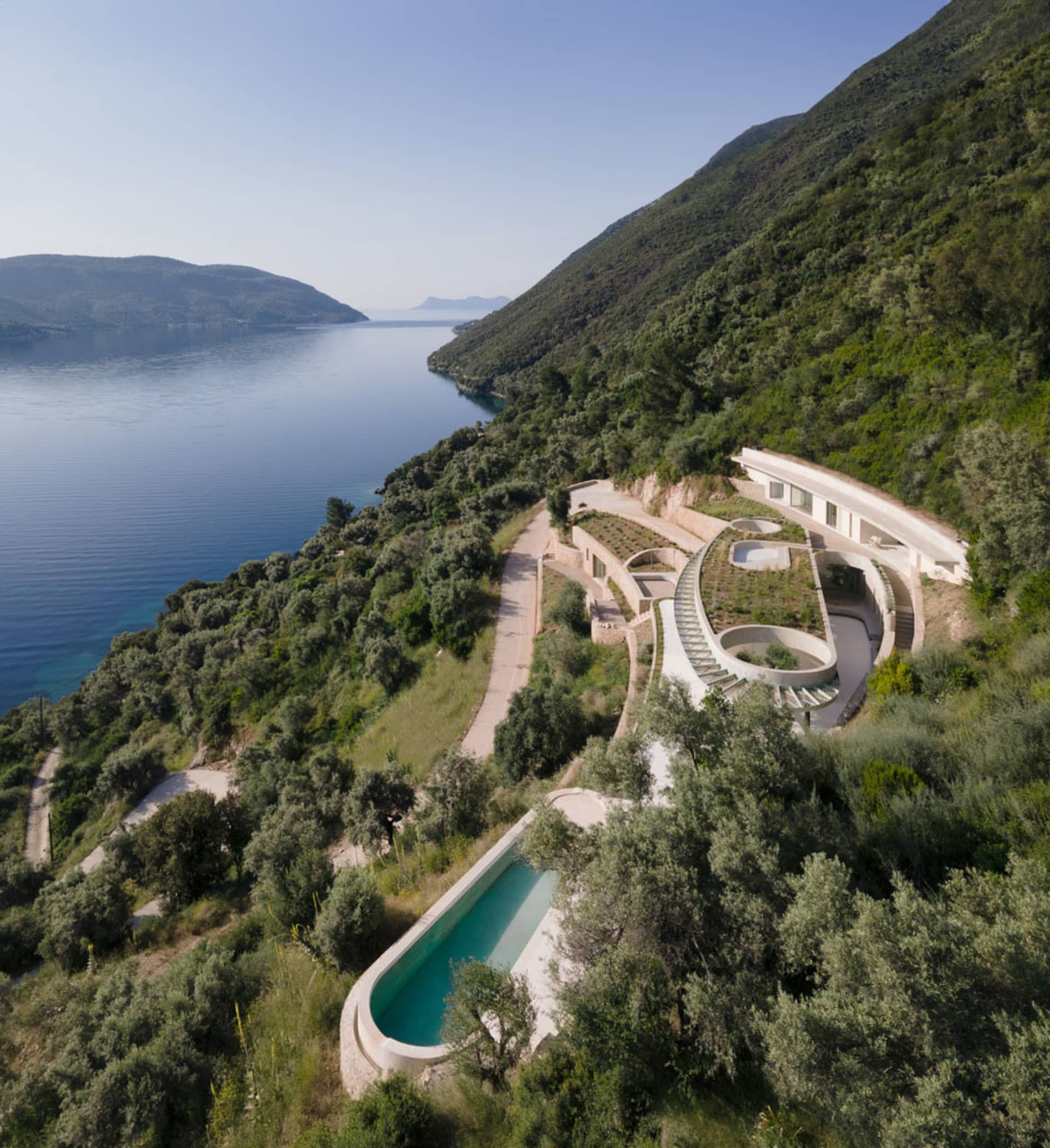 Modern pool with concrete terraces on a hillside overlooking a serene lake.