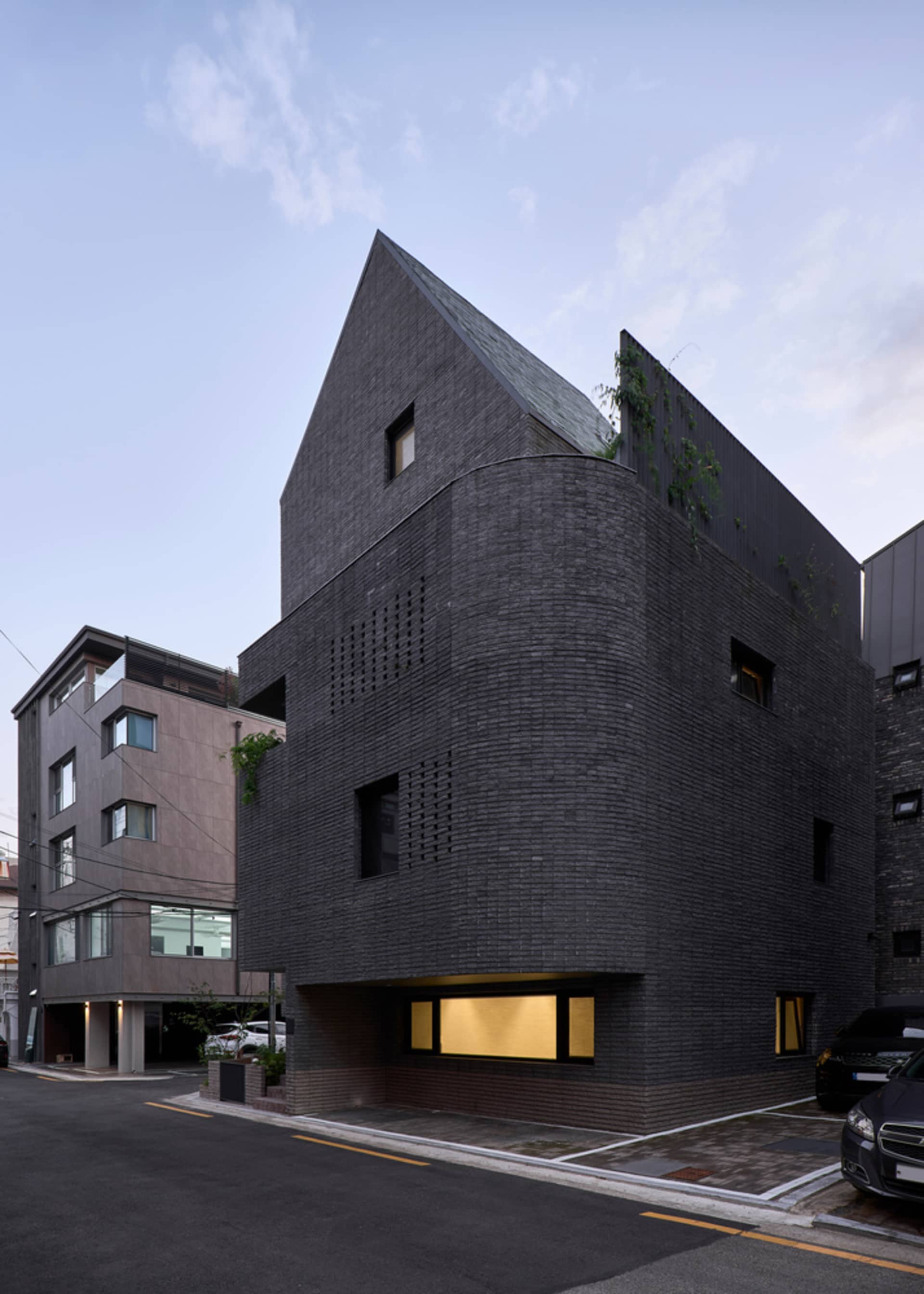 Modern architectural design featuring a black brick exterior with geometric windows and a sloped roof.