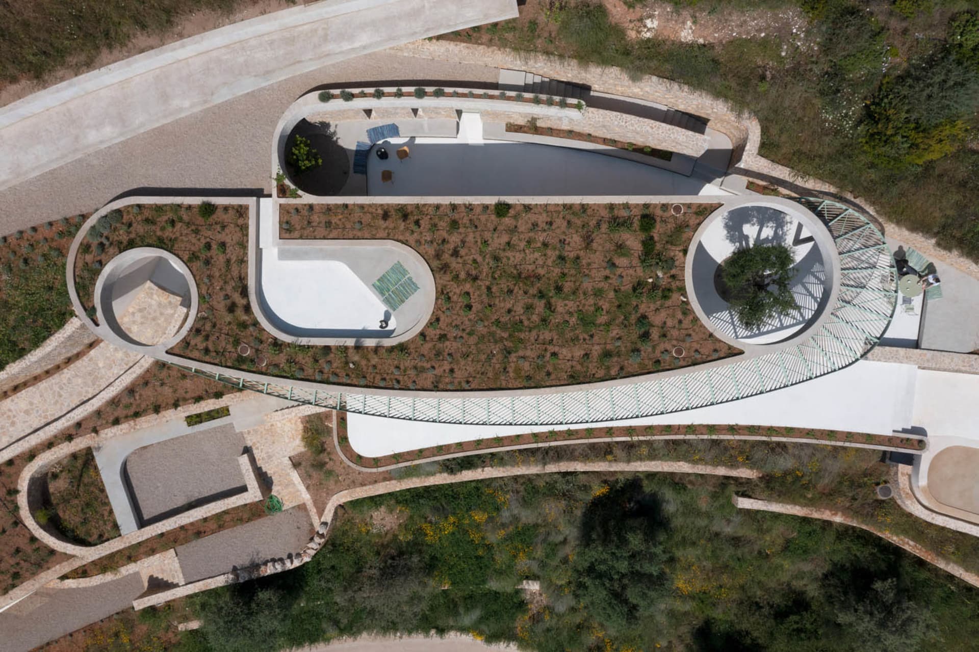 A modern park landscape with concrete pathways, stone walls, and lush green plants.